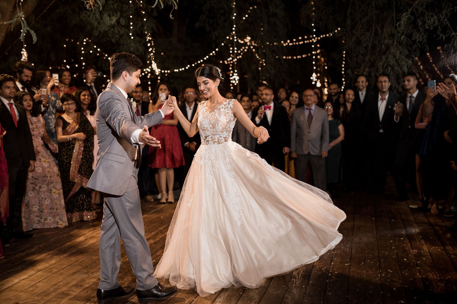 Bride and groom share their first dance under twinkling lights at an elegant outdoor evening wedding reception.