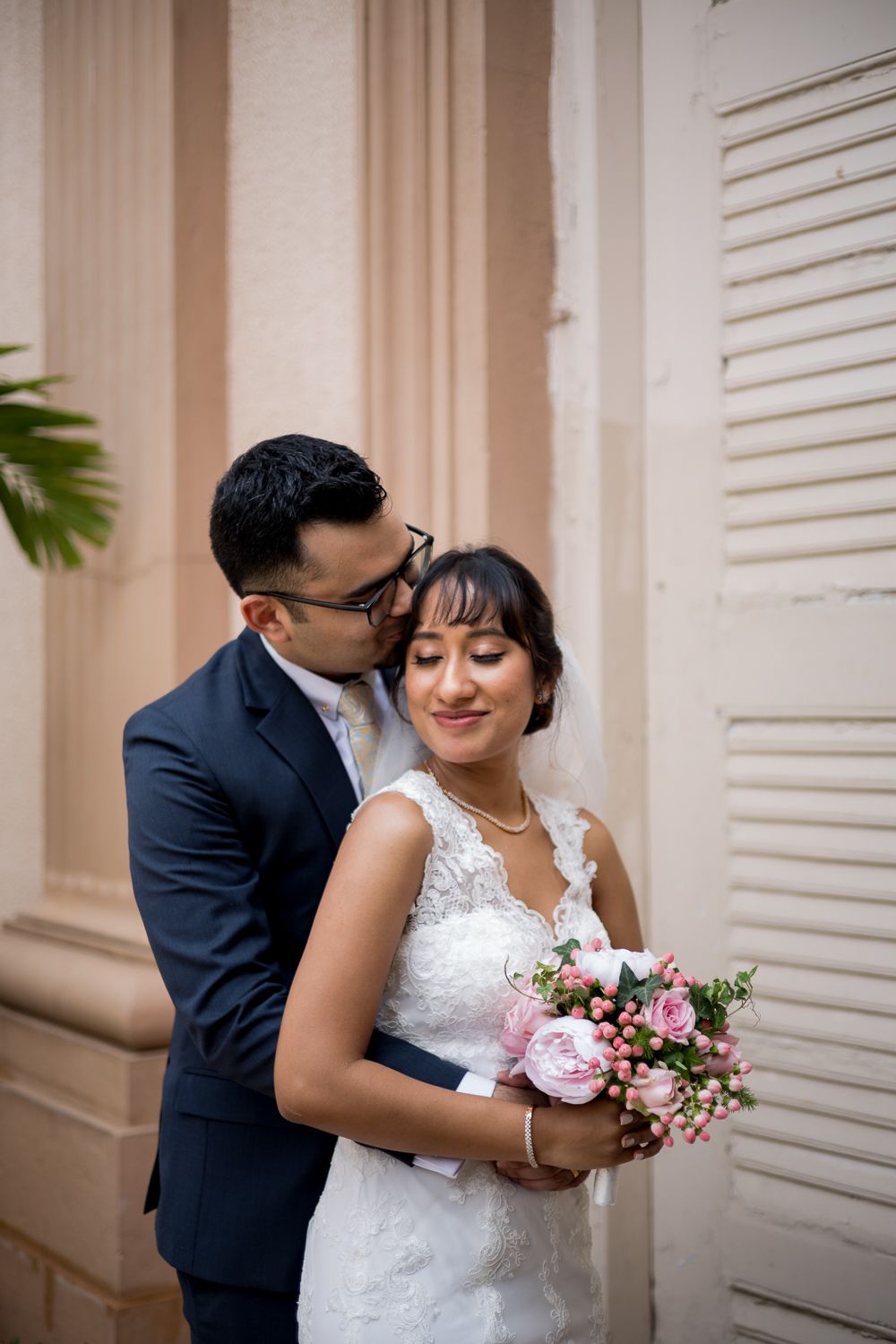 A romantic wedding couple shares intimate moments in a series of four photos against a light-colored wall with shutters.