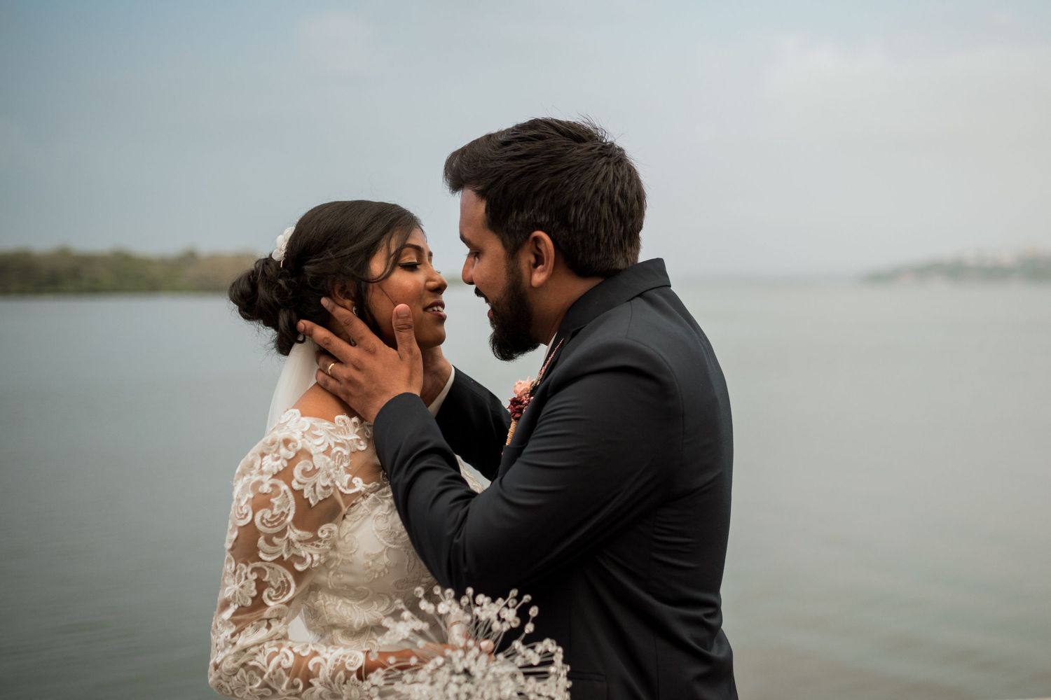 Intimate moment between couple by waterfront in formal wedding attire.