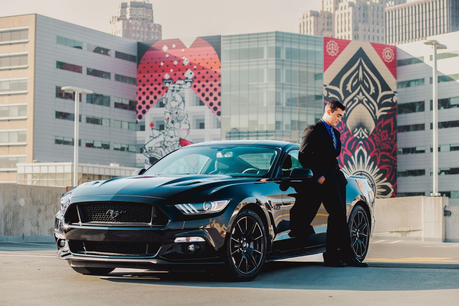Luxury sports cars parked against modern urban architecture with colorful murals.