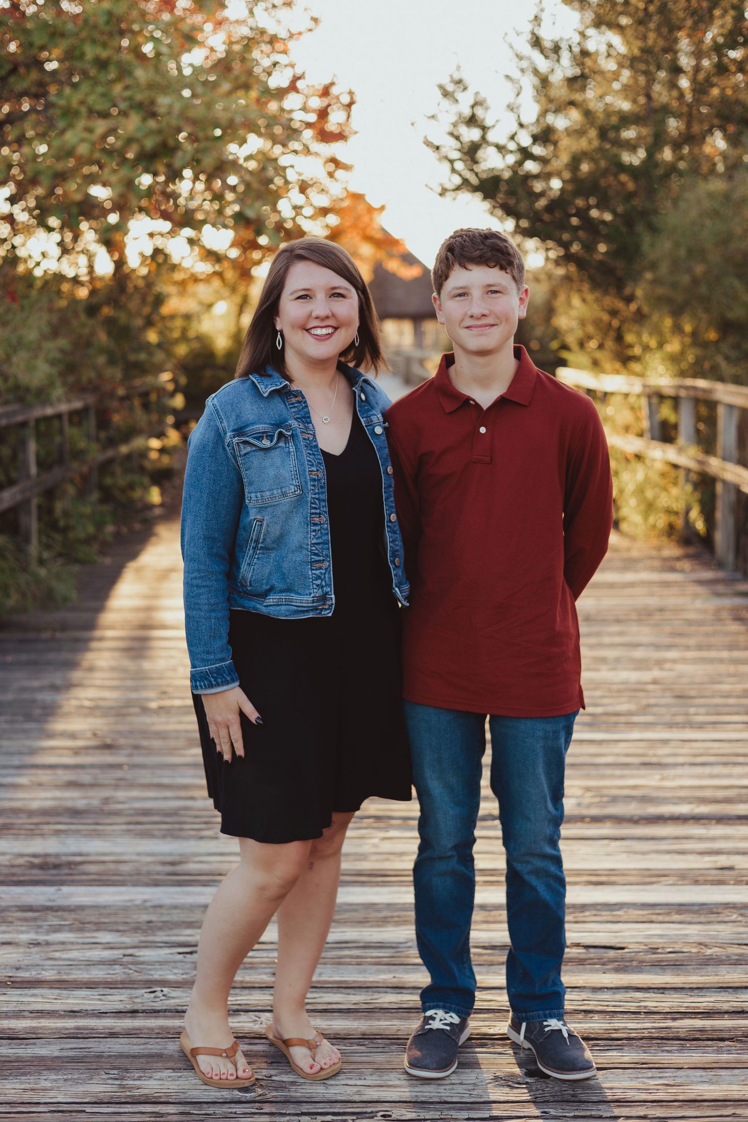 Two people posing together on wooden boardwalk during golden hour in autumn setting.