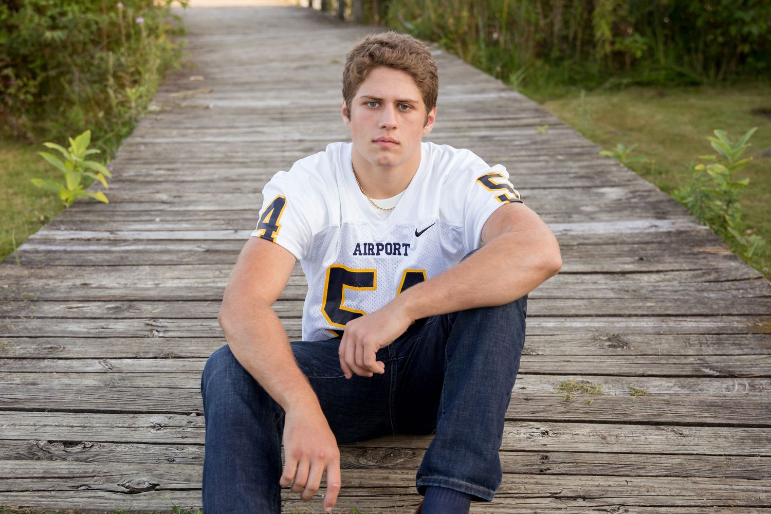 Senior portraits on wooden boardwalk surrounded by lush greenery.