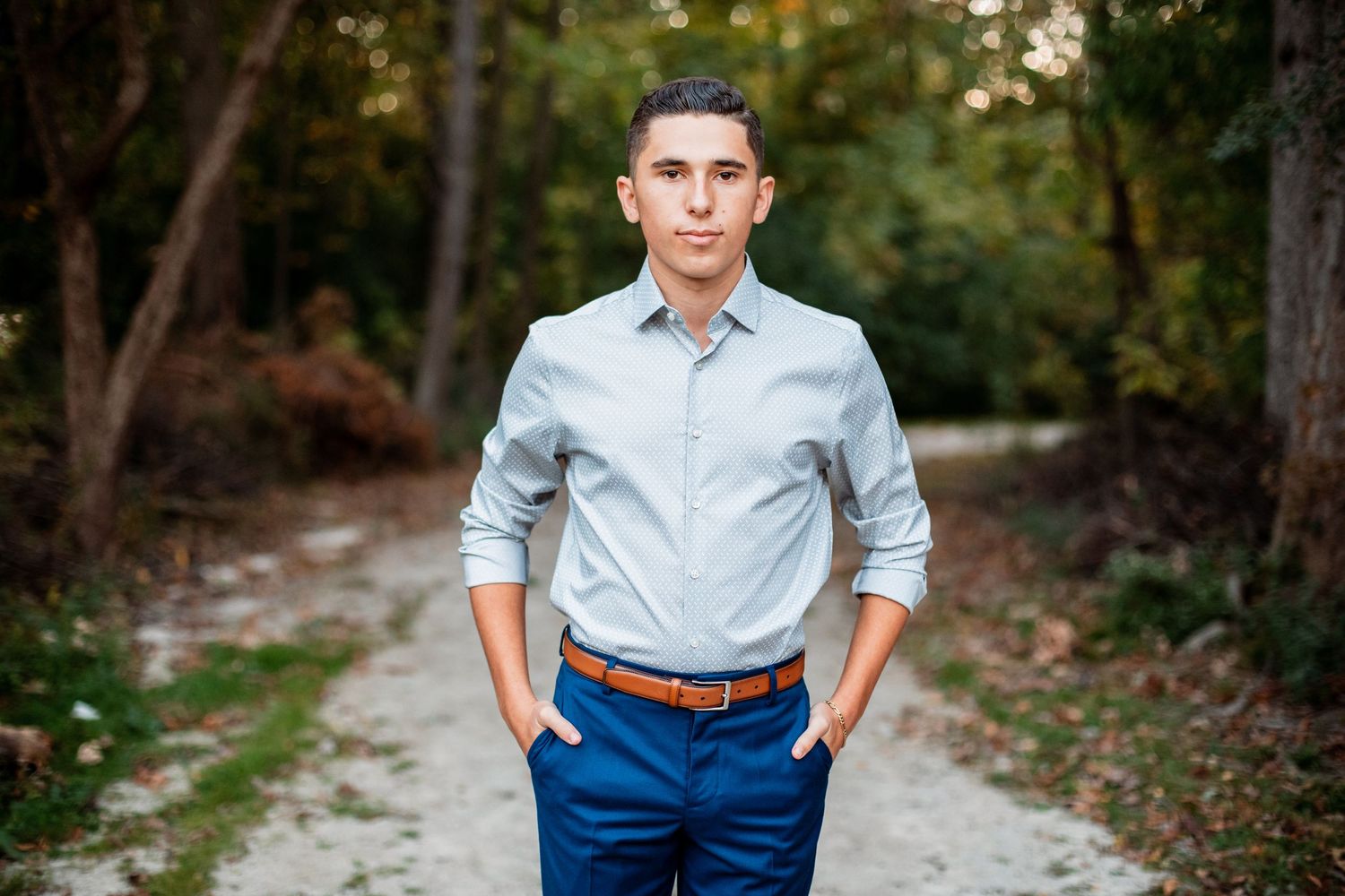 Professional casual portrait on nature path wearing light blue shirt and navy pants.