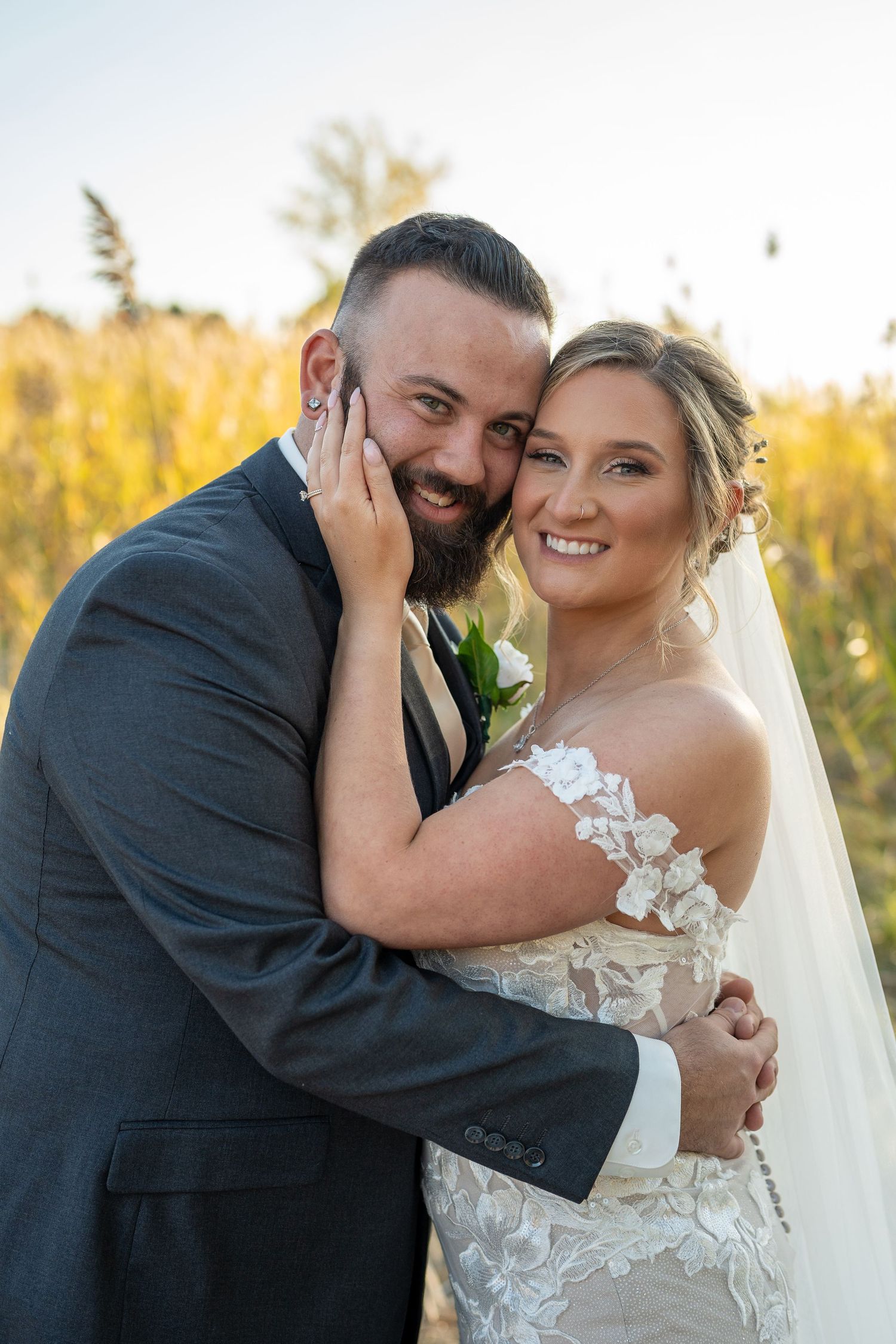 A happy couple embraces outdoors on their wedding day with golden autumn foliage in the background.