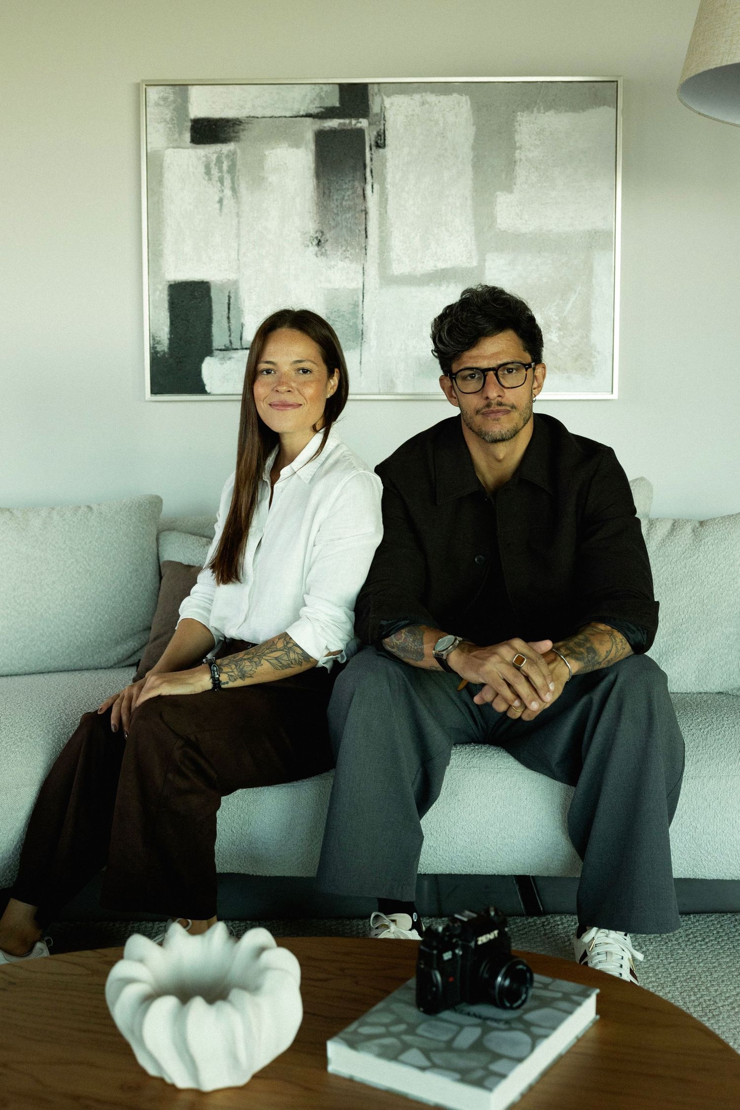 A man and woman sitting together on a gray sofa in front of abstract wall art in a modern living room.