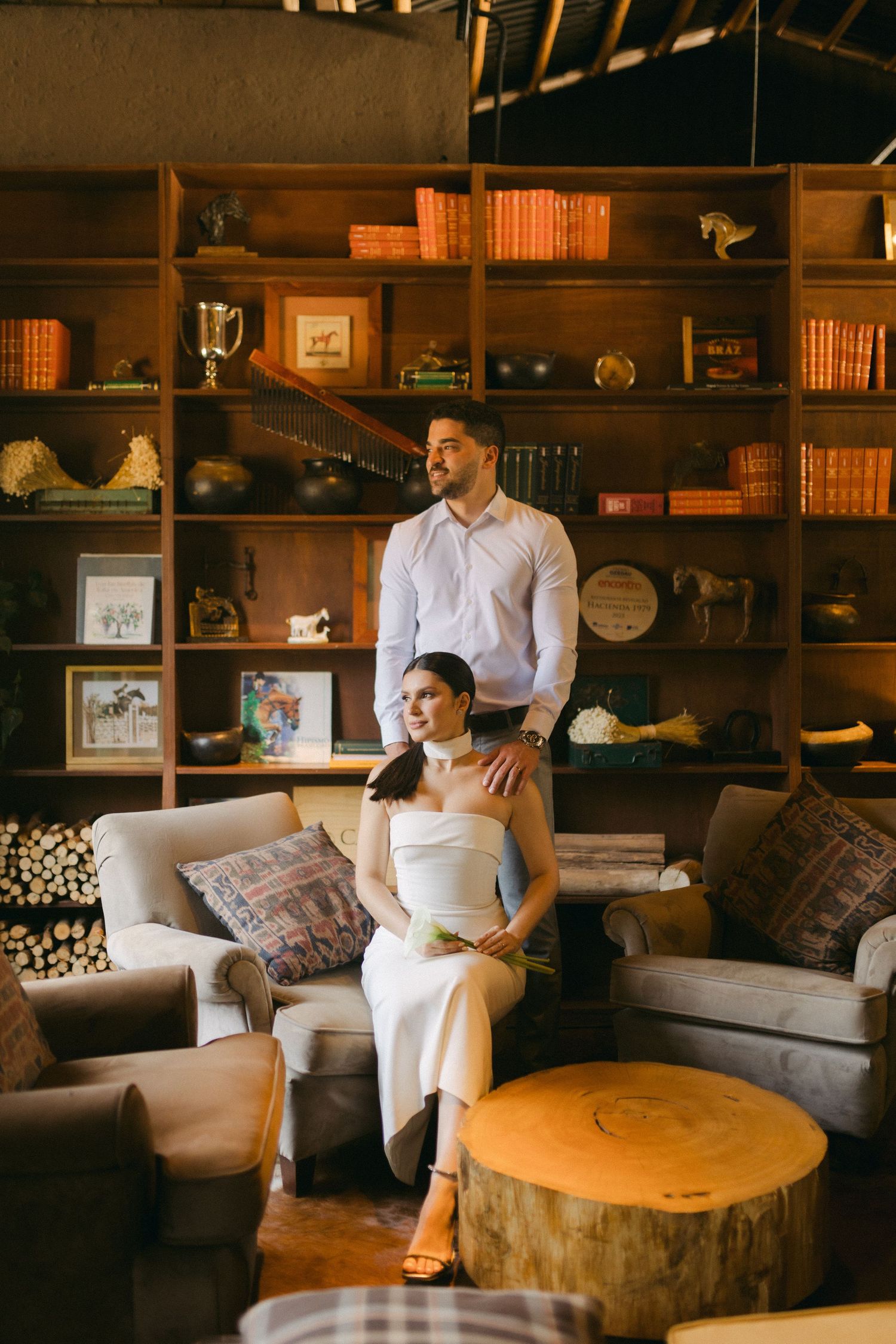 Elegant couple posing in cozy living room with vintage bookshelf and wooden decor.