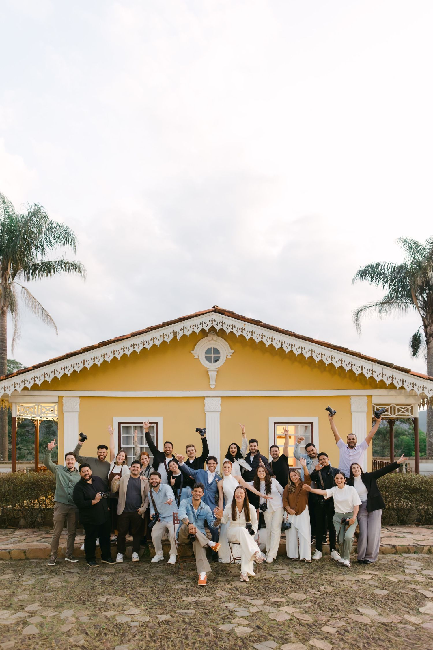 Wedding party group poses together in front of a yellow Spanish-style building for celebratory photos.