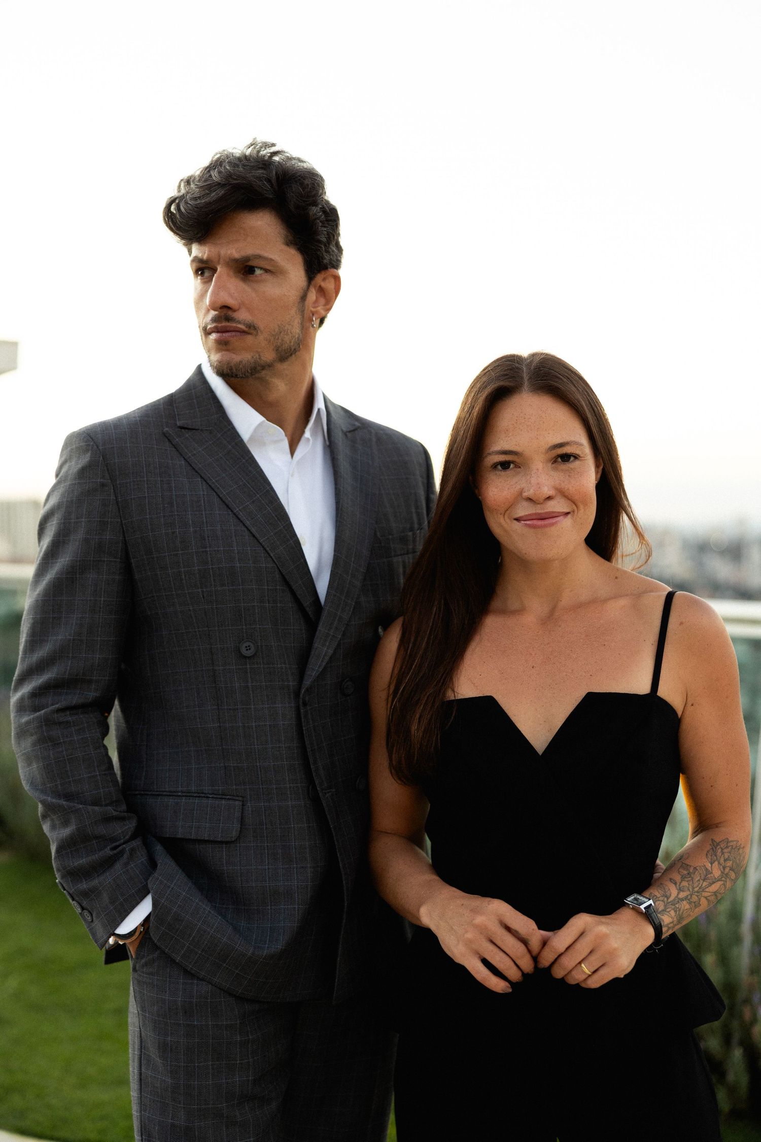 A man in a gray suit and woman in a black dress pose together outdoors at a formal event.
