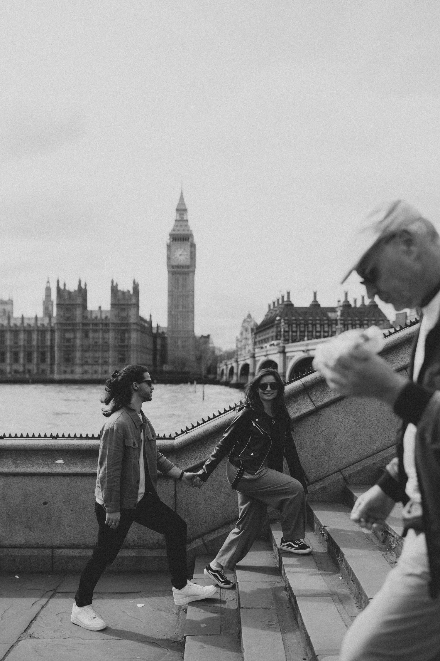 Tourists pose playfully near Big Ben and Houses of Parliament in London in black and white photography.