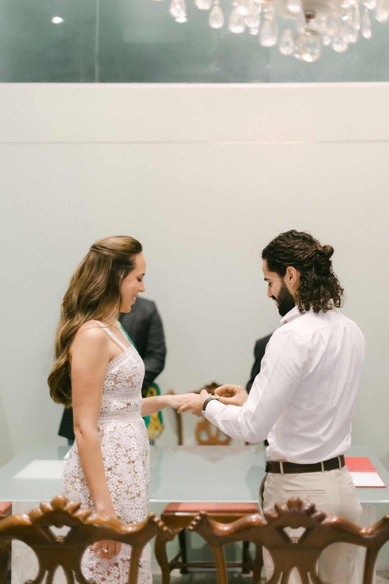 An intimate moment during a ring exchange ceremony under crystal chandelier lighting.