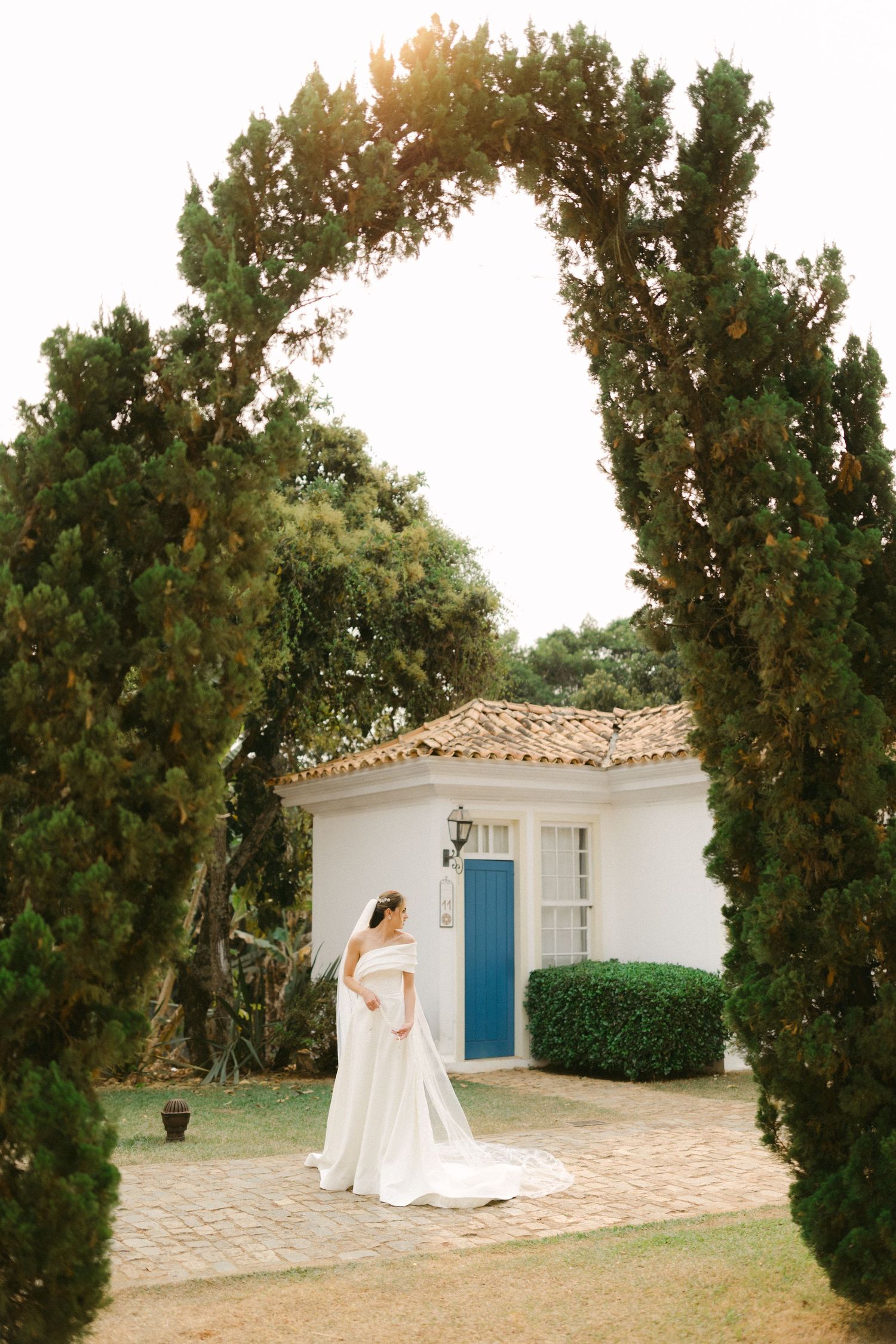 A white Mediterranean-style building with blue shutters and cypress trees creates a romantic outdoor setting.
