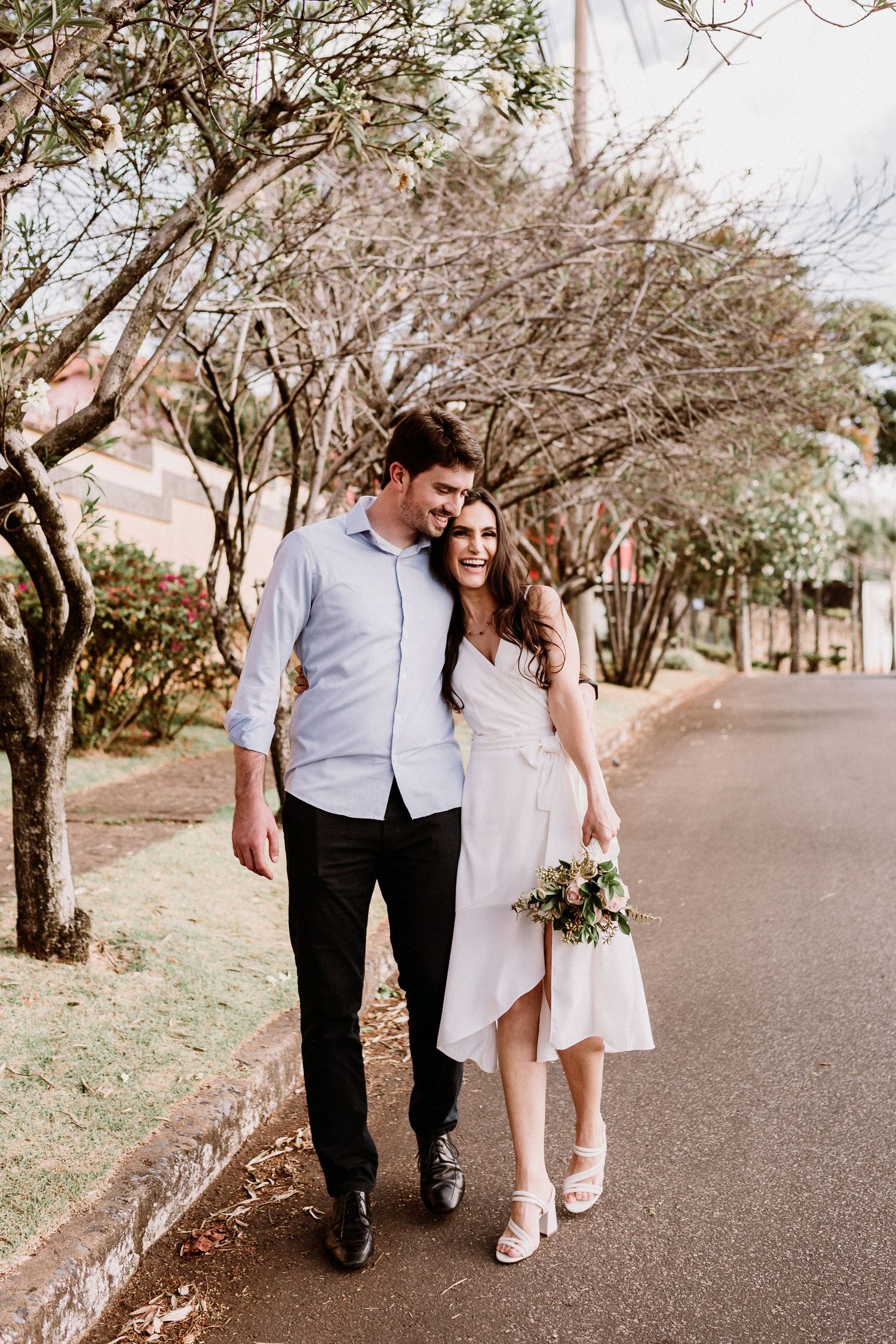 Couple walking together on tree-lined path in casual wedding attire.