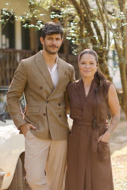 A couple in vintage-style clothing poses together outdoors in autumn, wearing brown and beige coordinated outfits.