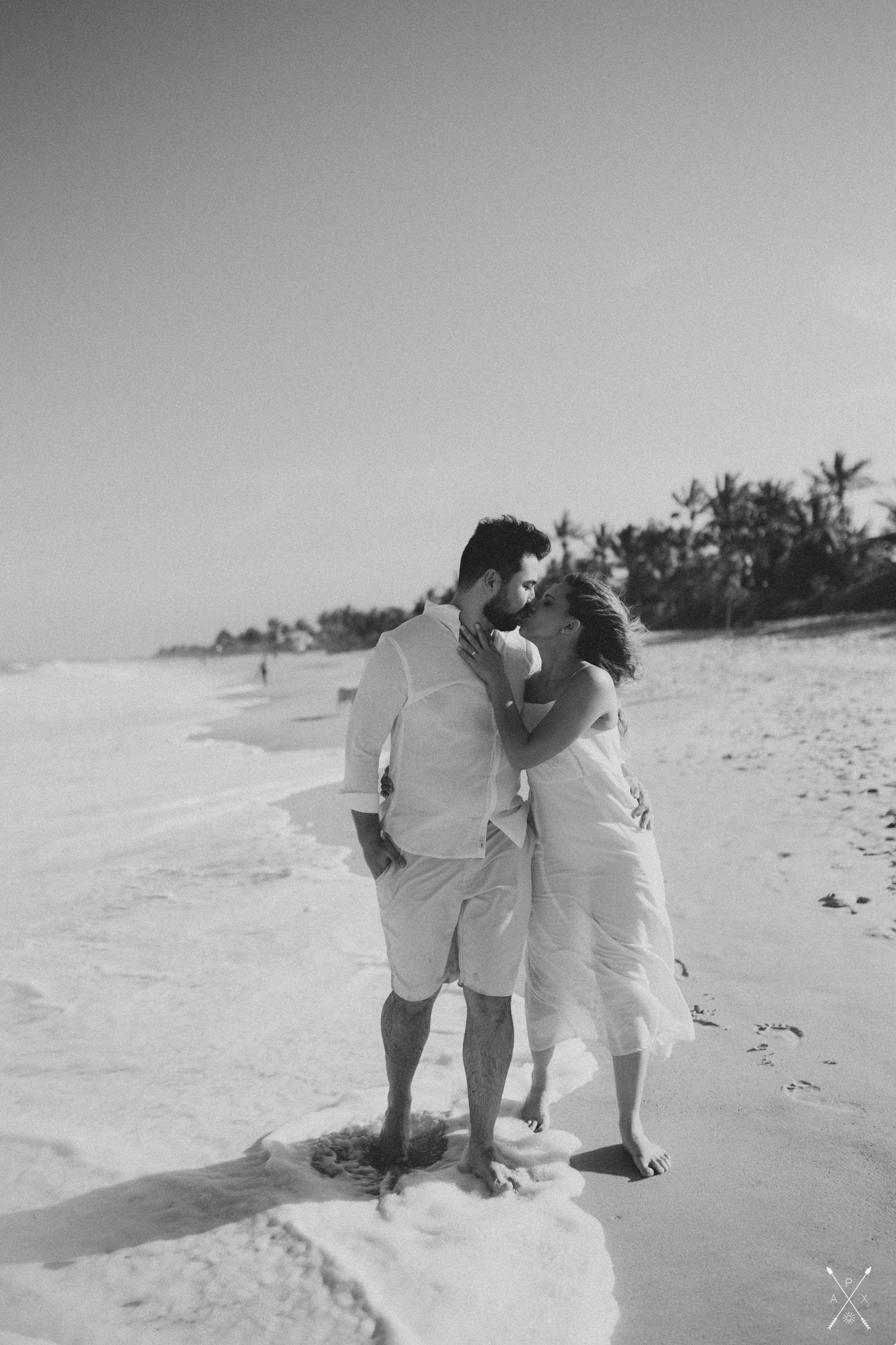 A black and white beach photo of a couple sharing an intimate moment by the ocean.