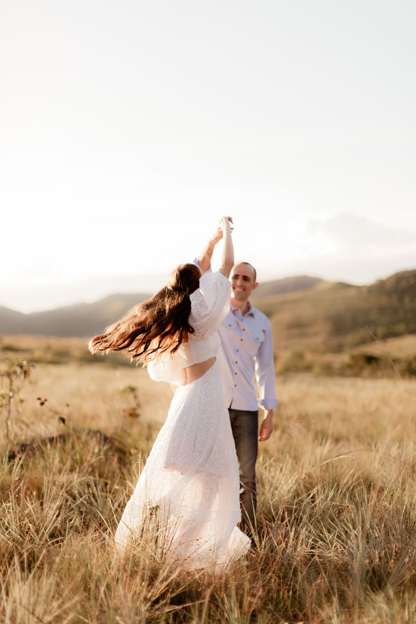 A couple dances in a field of tall grass during golden hour in the mountains.