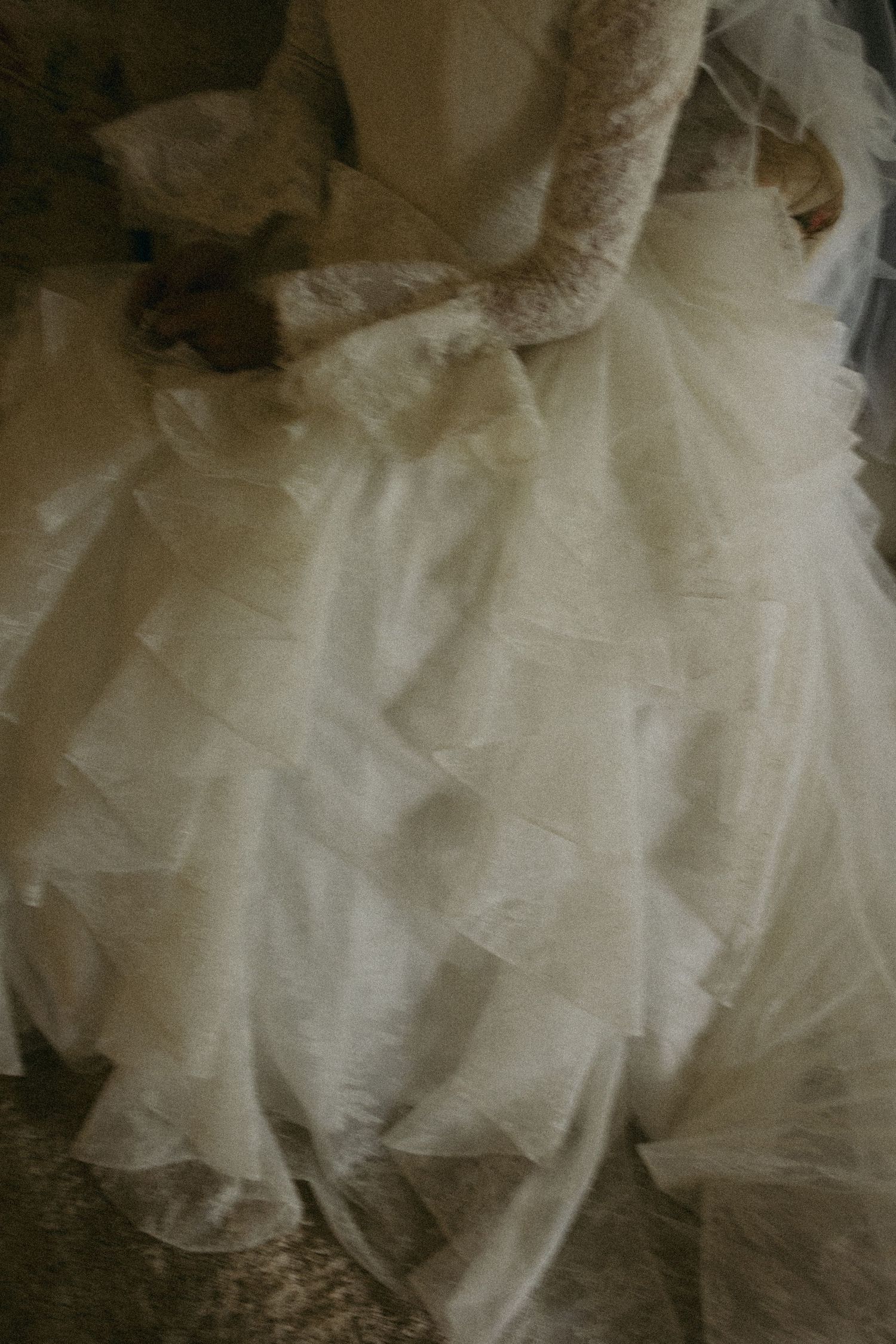 Bride in a layered white tulle and lace wedding gown with long sleeves, holding the skirt of her dress.