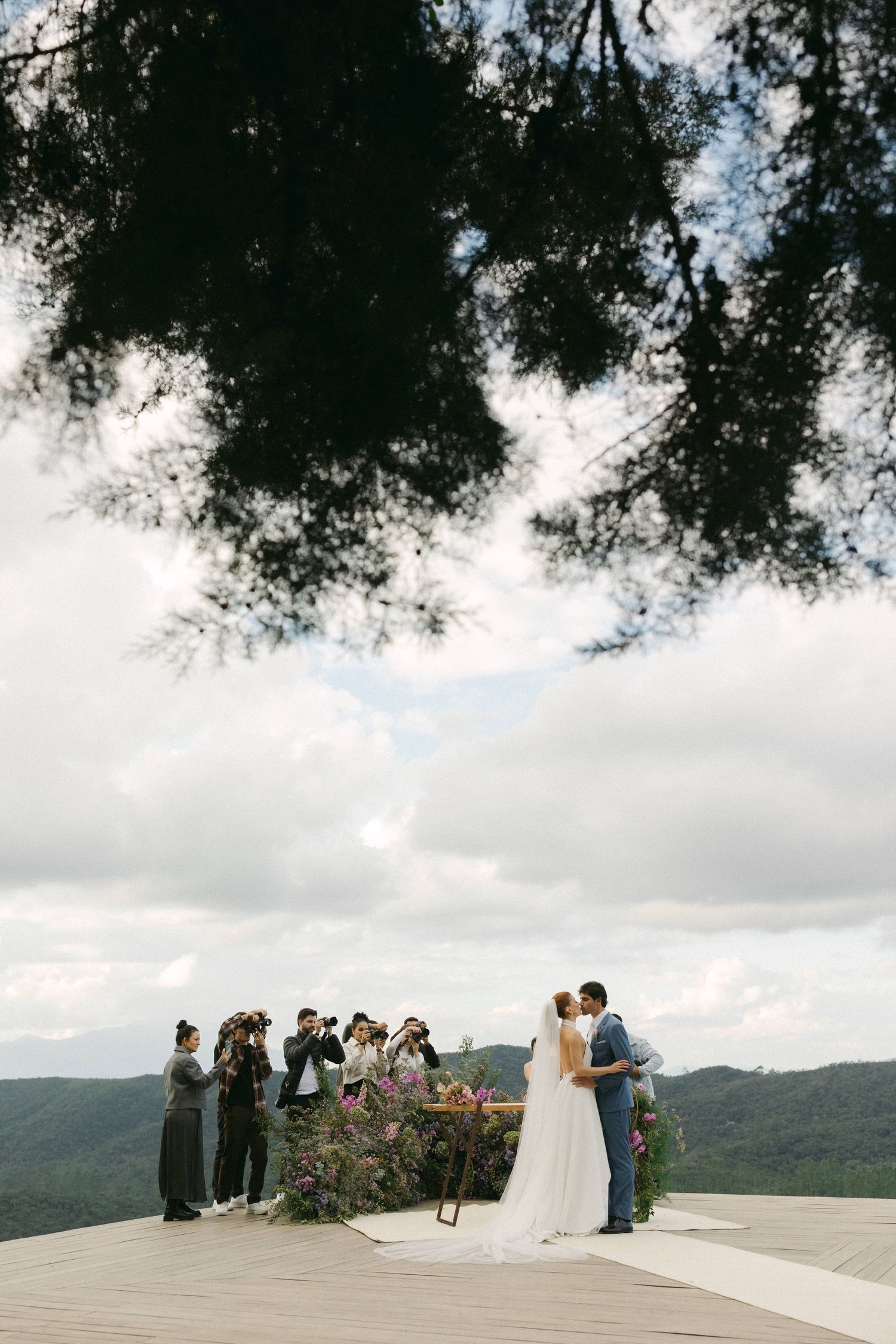 Wedding ceremony taking place on a scenic mountain overlook with guests gathered under cloudy skies.