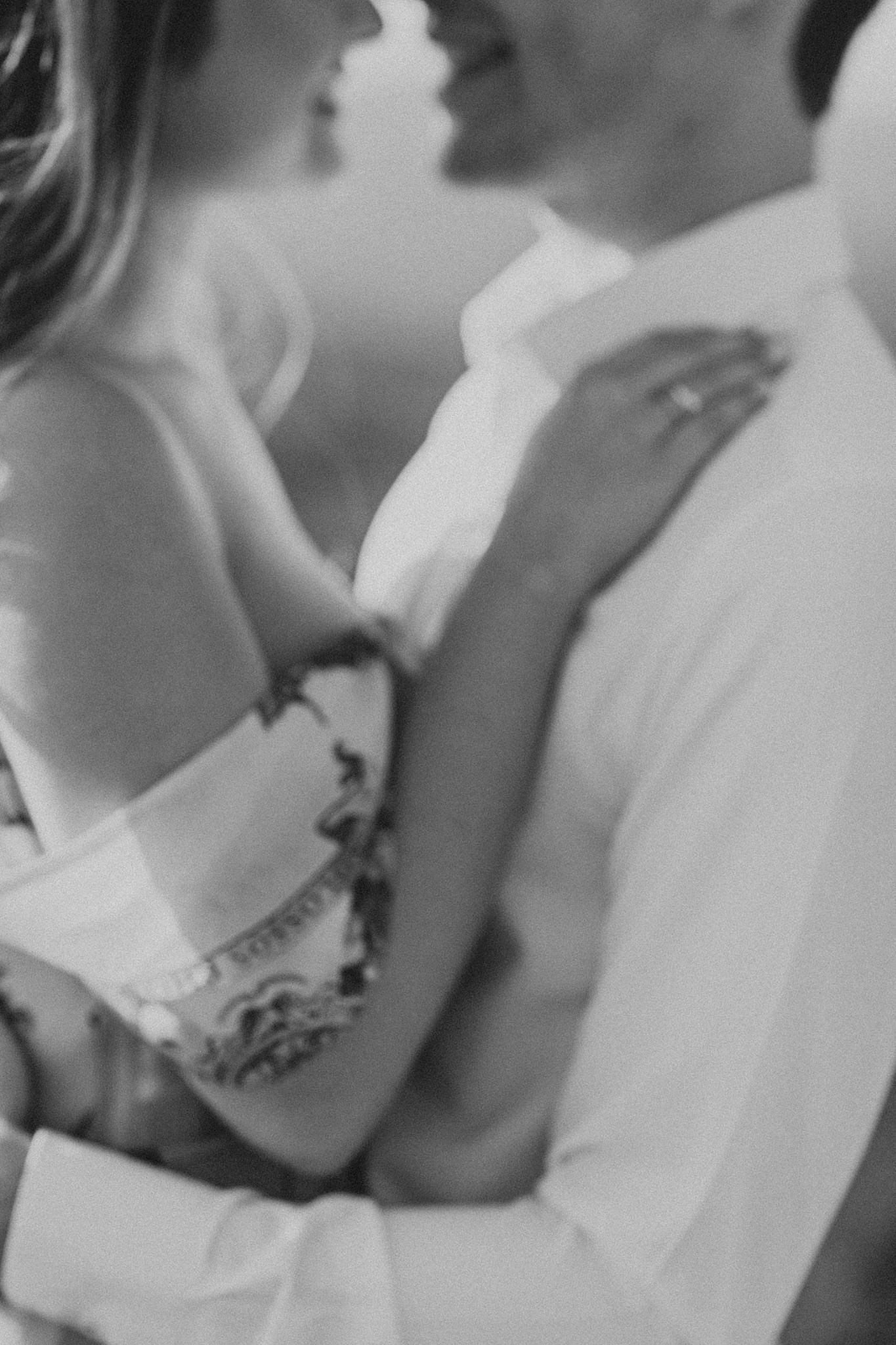 An intimate black and white close-up of a couple in white formal attire.