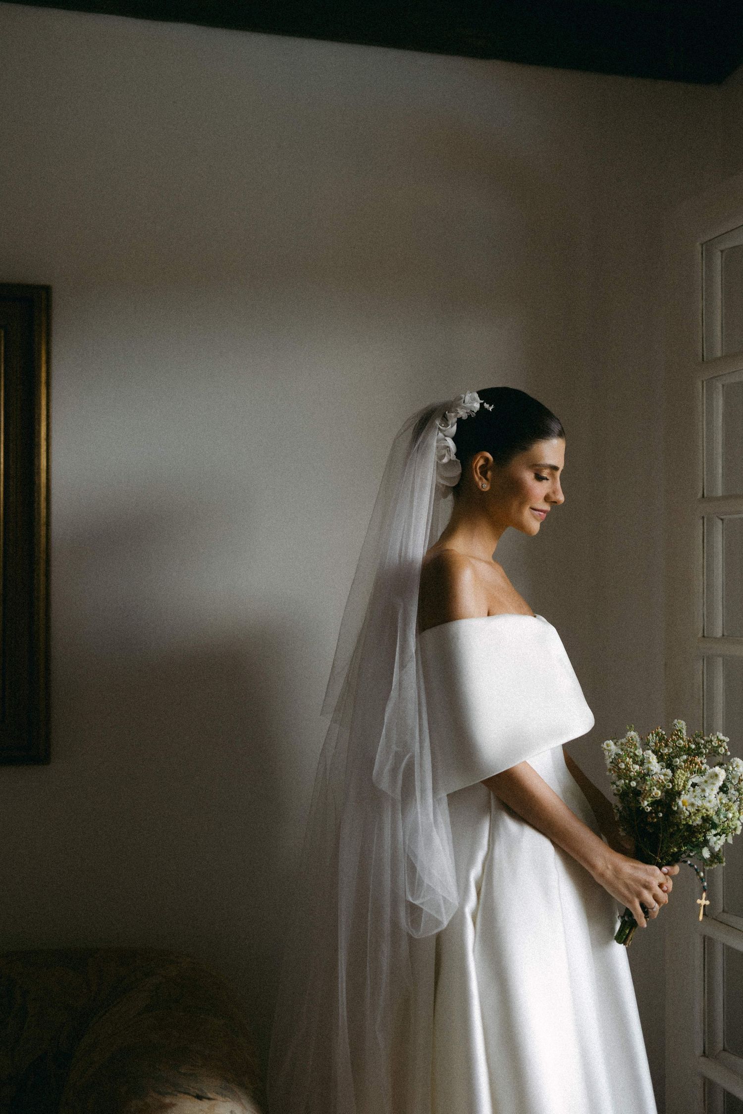 Classic white wedding dress with veil captured in elegant window light creating a serene bridal portrait.