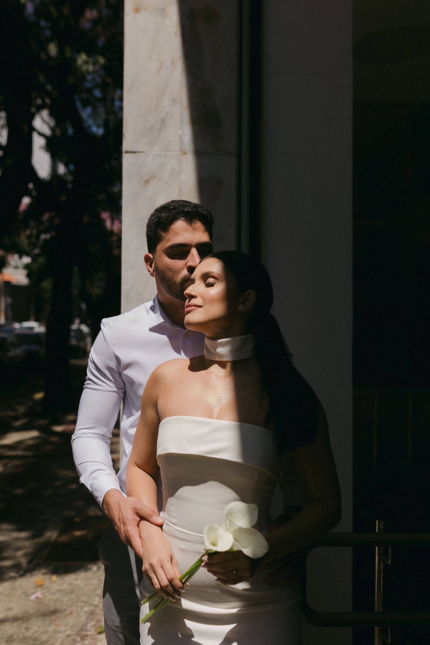 Romantic portrait of couple in formal attire embracing in shadowed doorway.