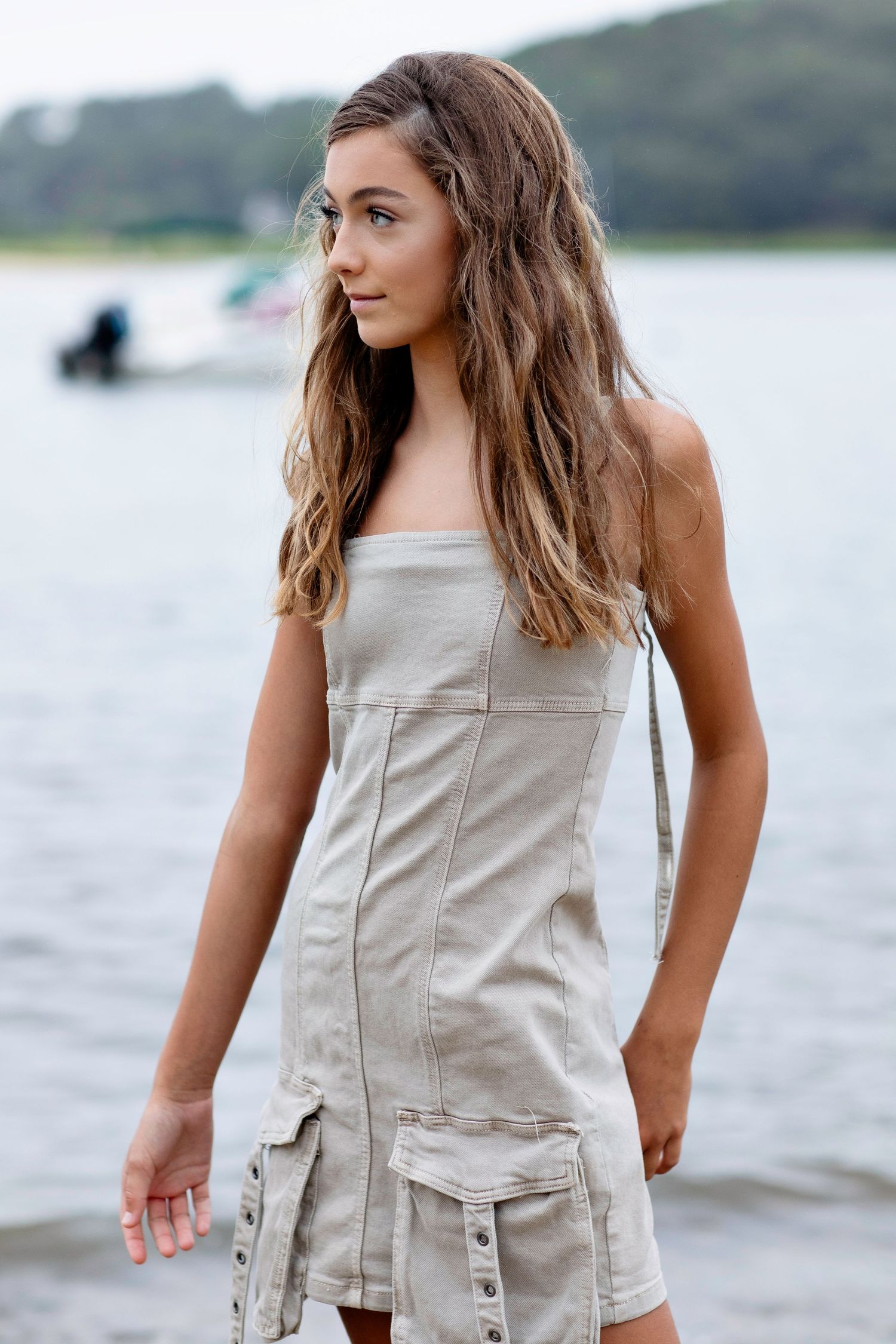 Person in a beige strapless utility dress poses outdoors near a waterfront.