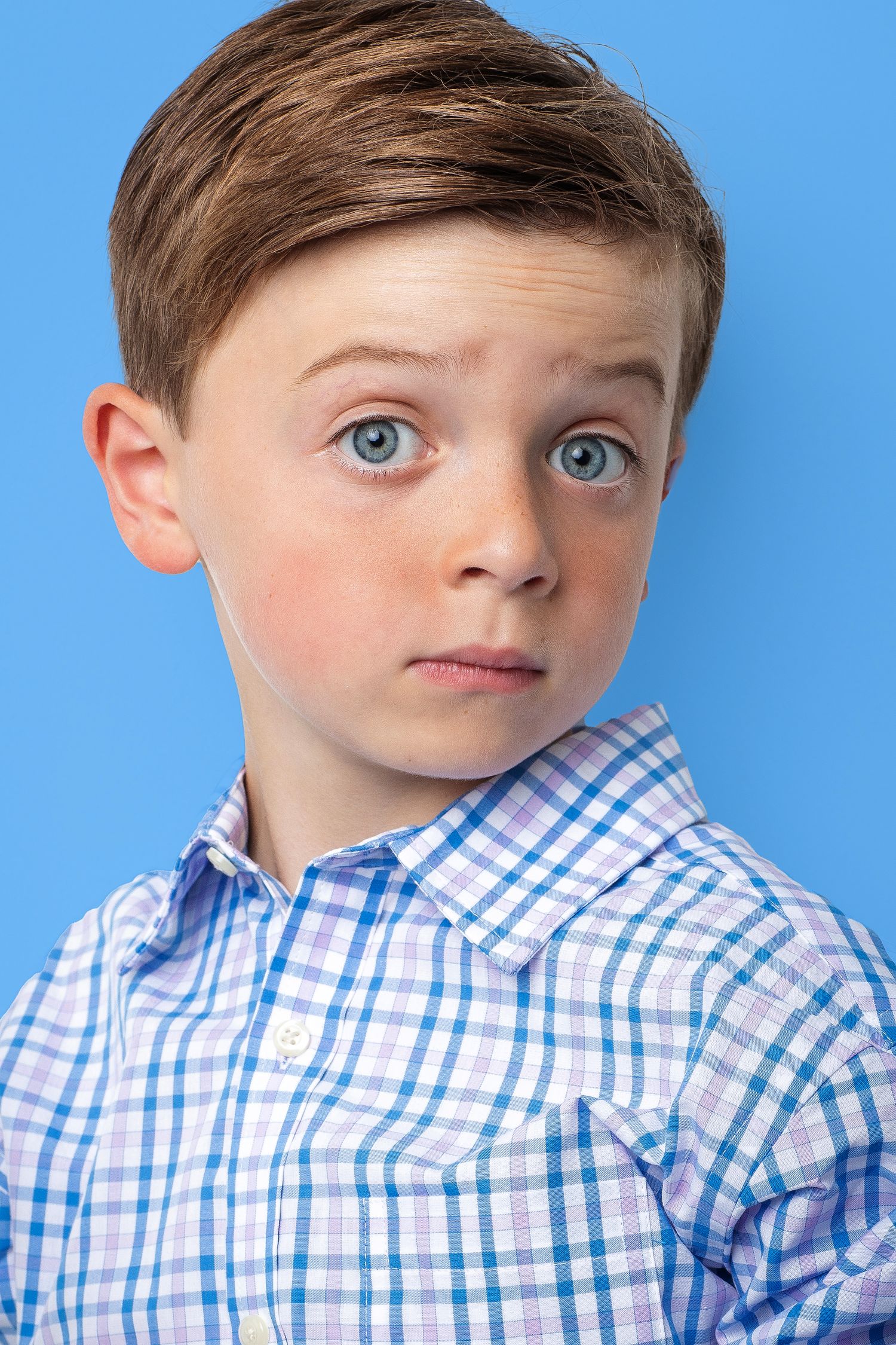 Young talent in blue and white checkered shirt against bright blue background.