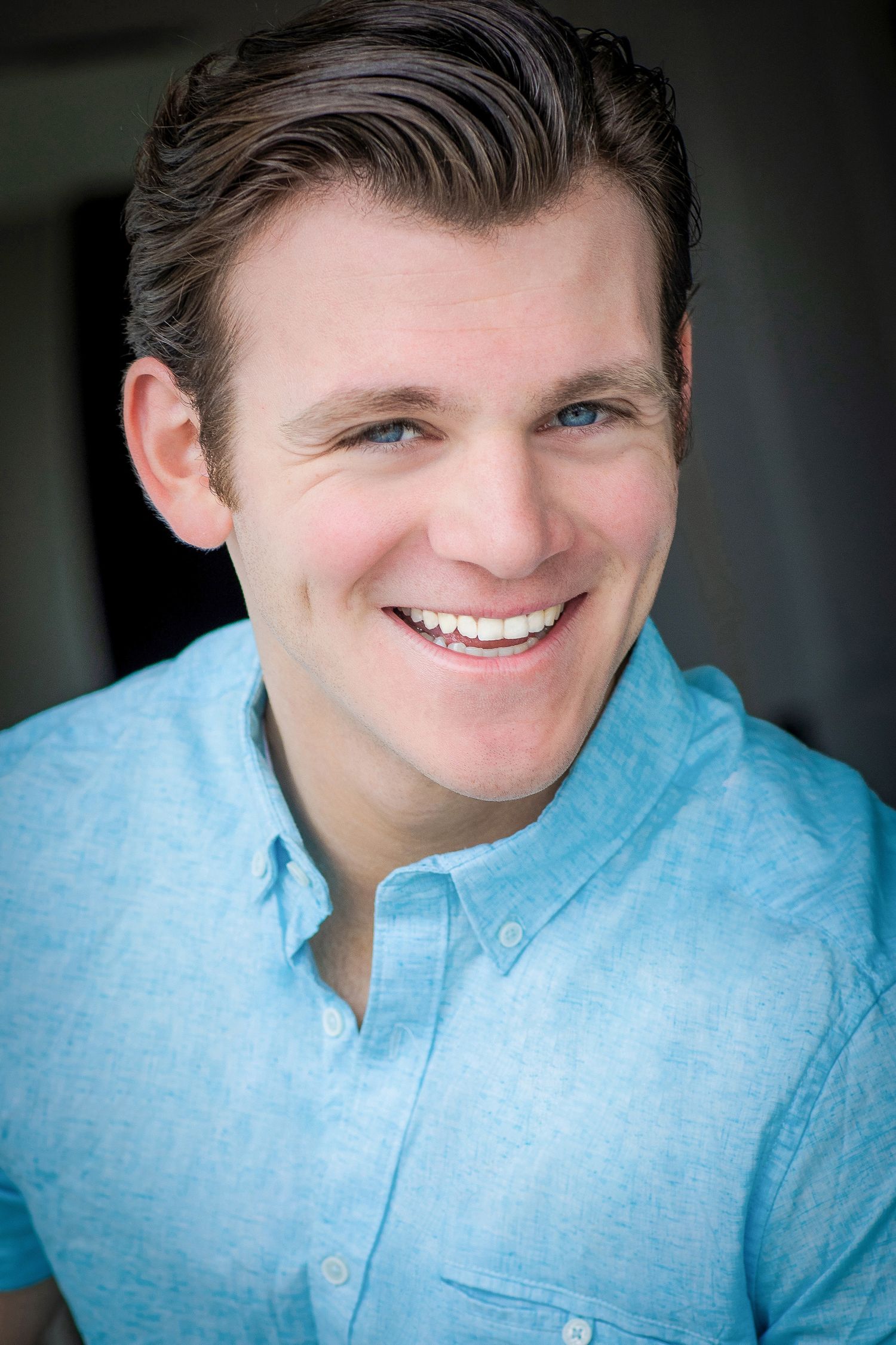 Professional headshot of person in light blue button-down shirt with friendly smile.