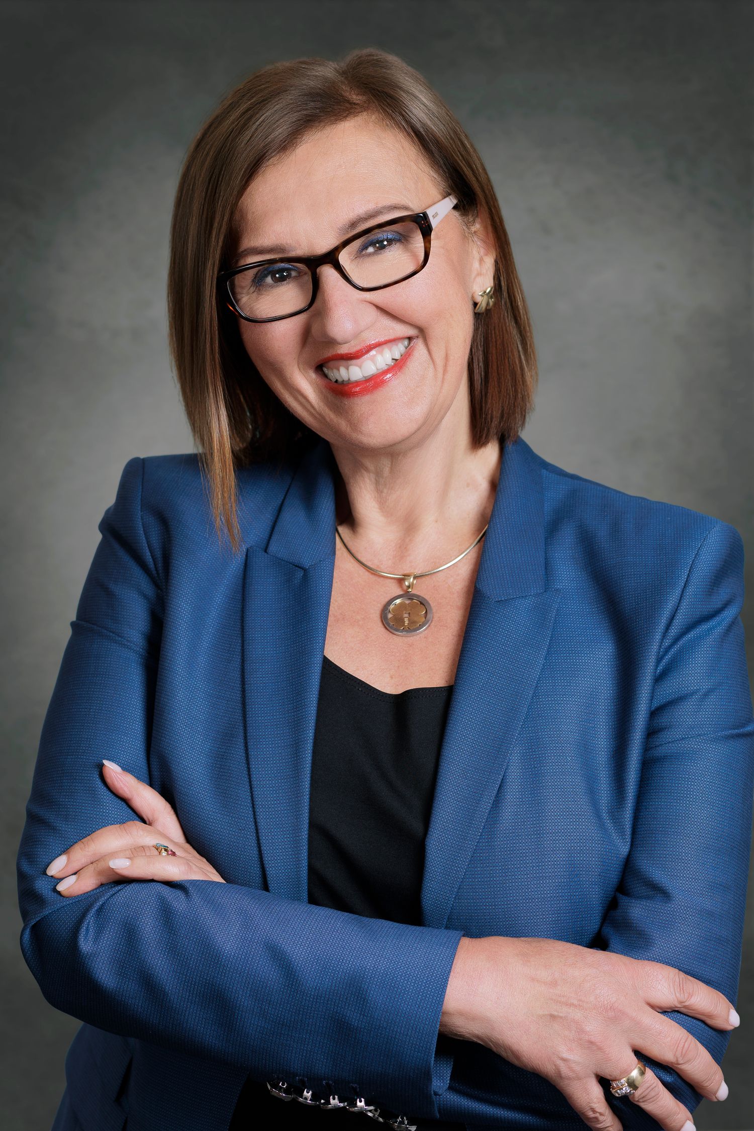 Professional woman in blue blazer and glasses smiling with arms crossed against gray background. Wollongong Headshot Photographer