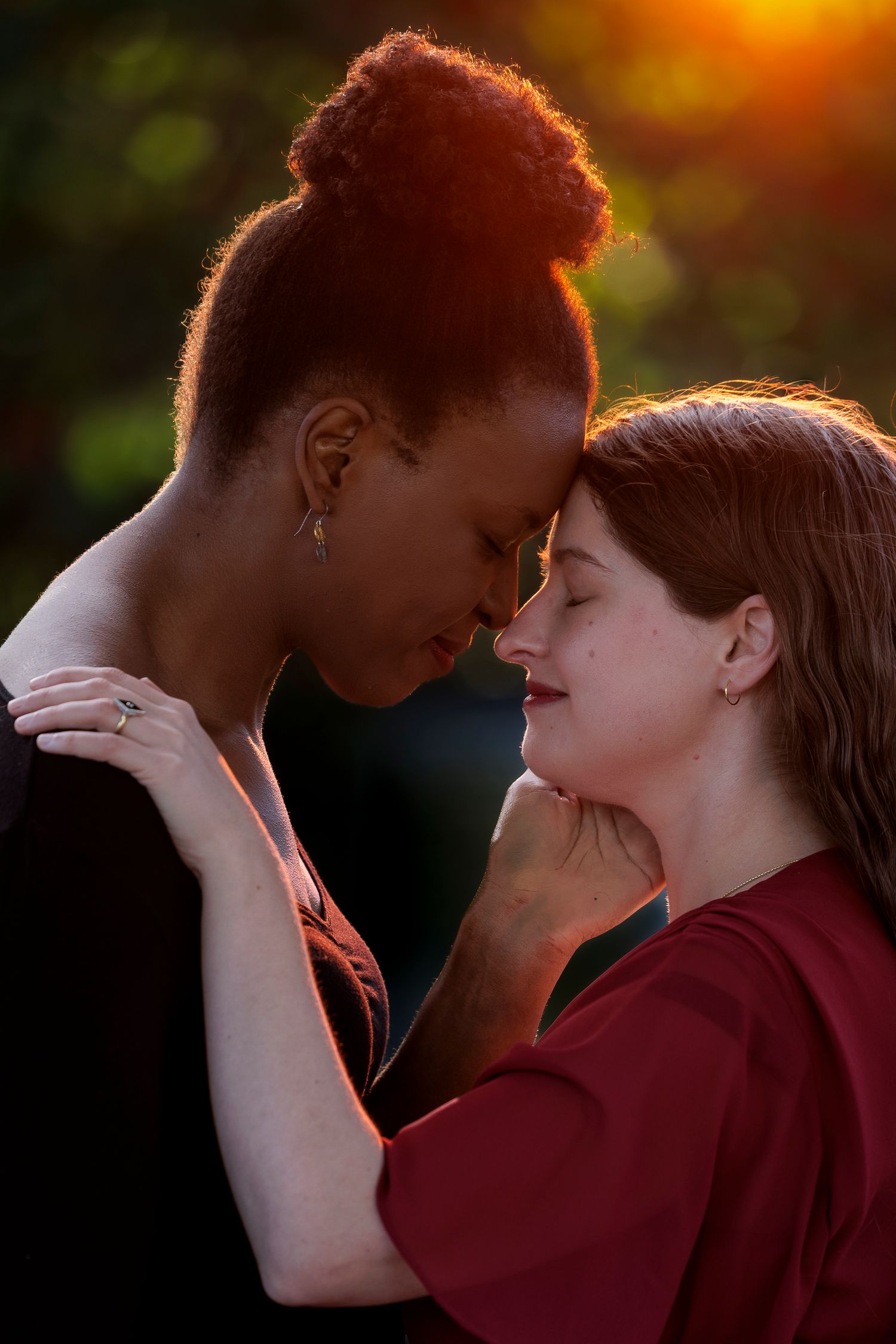 Two women sharing an intimate moment outdoors, foreheads touching, bathed in warm golden sunset light. Wollongong Engagement Photographer
