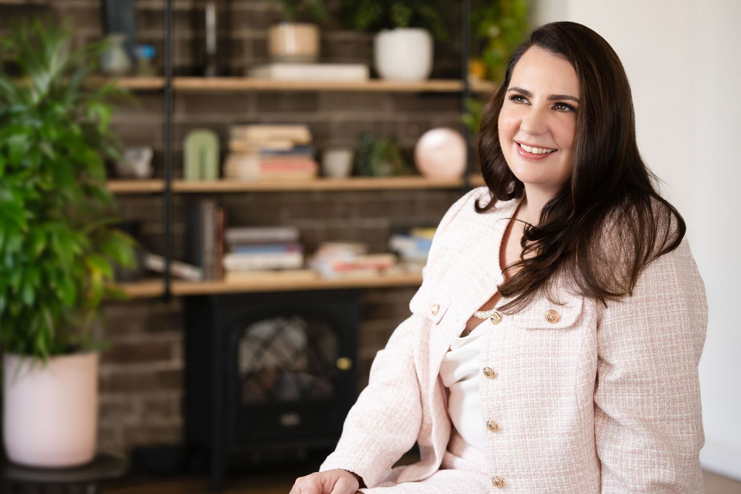 Smiling woman with dark hair in a pink tweed jacket seated in a modern living room. Wollongong Personal Branding Photography