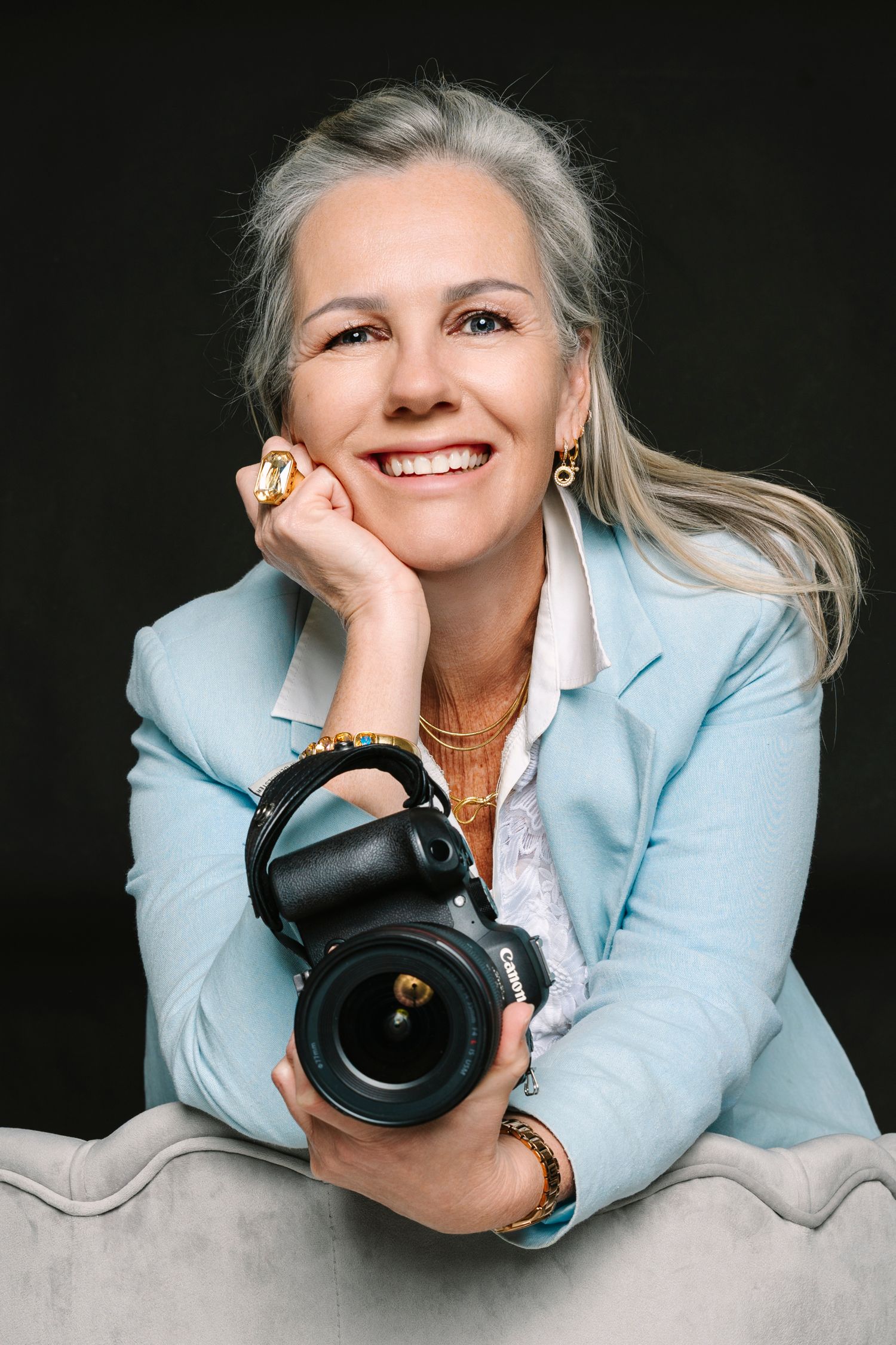 Smiling woman with gray hair in light blue blazer holding a professional camera. Wollongong photographer