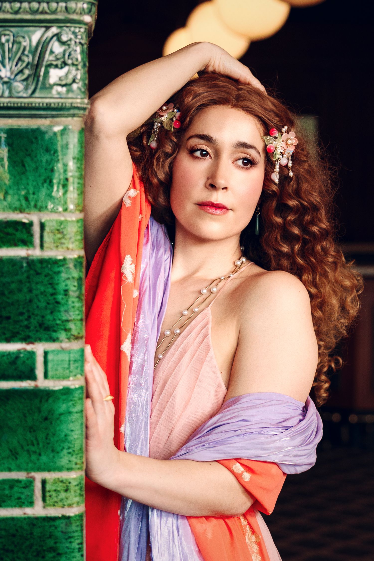 Wollongong Portrait Photographer. A woman with curly red hair adorned with flowers poses gracefully in colorful draped fabric.