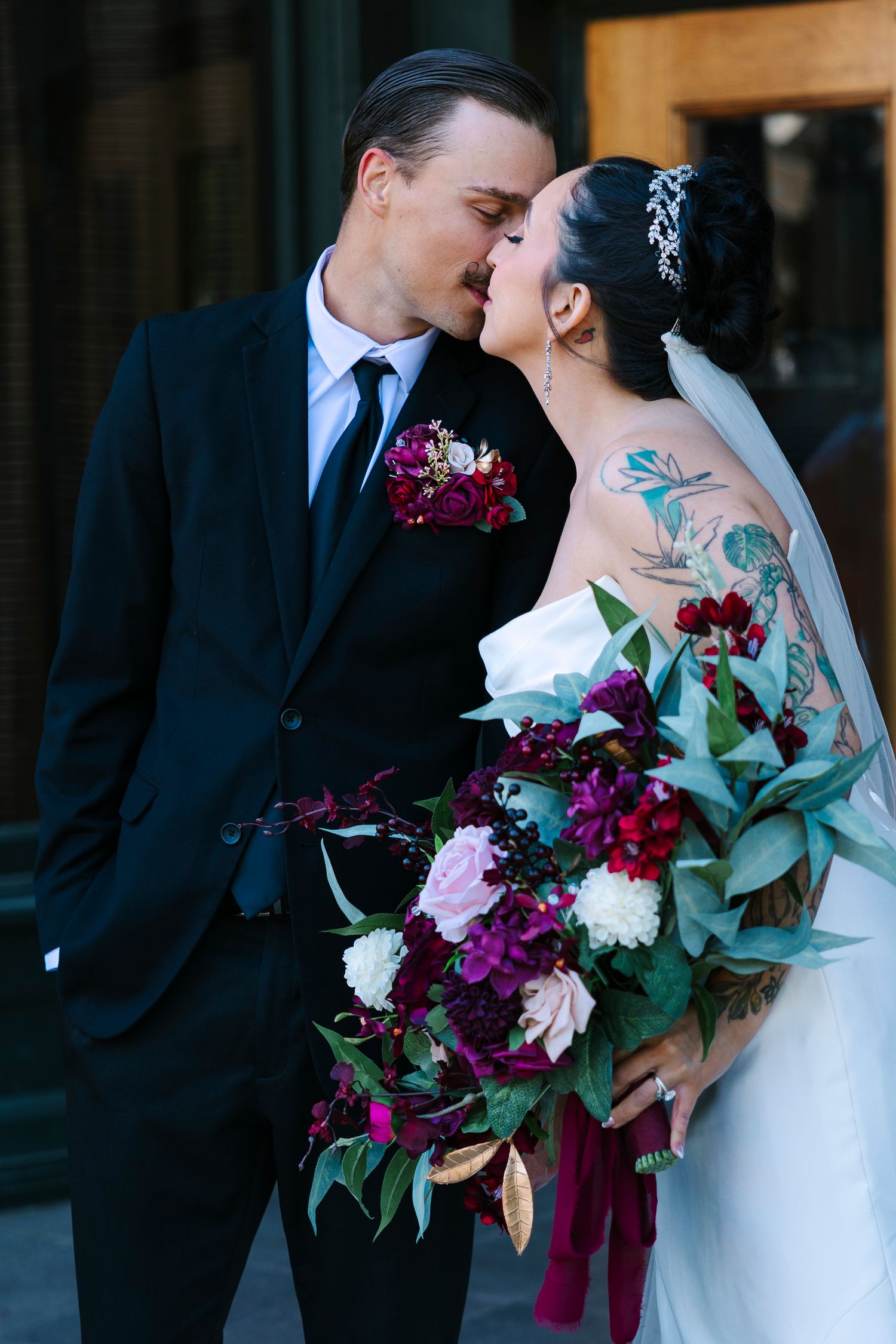 Bride and groom share a romantic kiss, bride holds a burgundy and pink bouquet. Wollongong Wedding Photographer