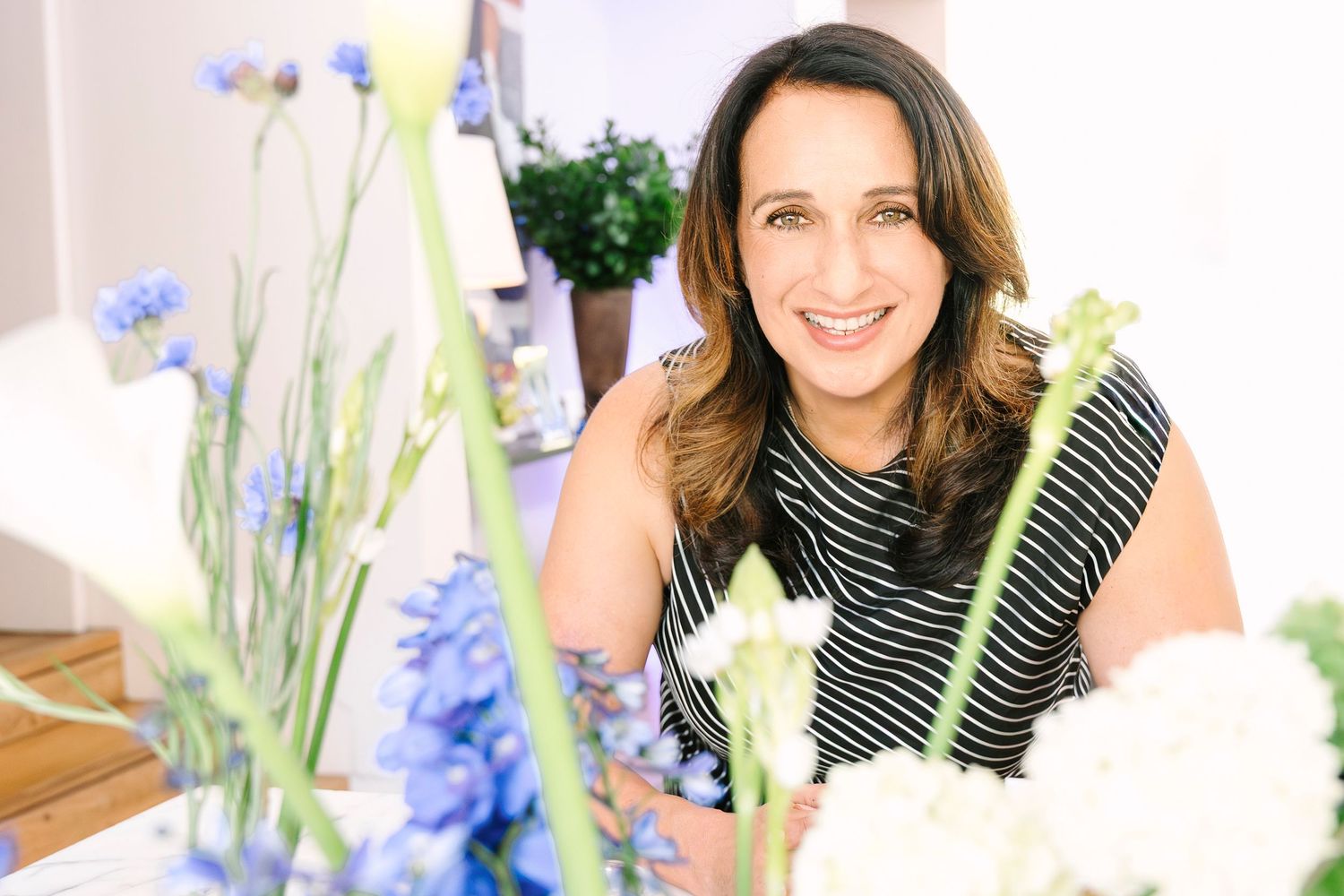 Smiling woman with brown hair posing among blue and white flowers in a bright studio setting. Wollongong Corporate Branding Photography