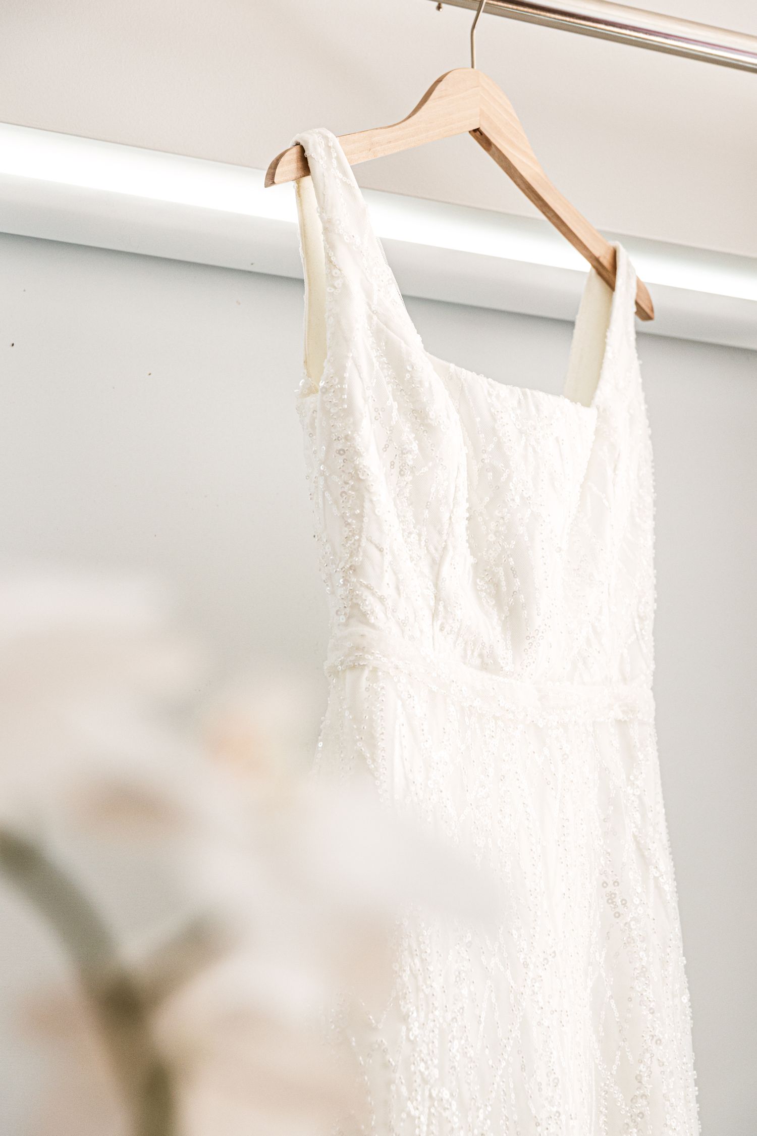 Wollongong Wedding Photographer.. White lace wedding dress hanging on a wooden hanger against a soft white background.
