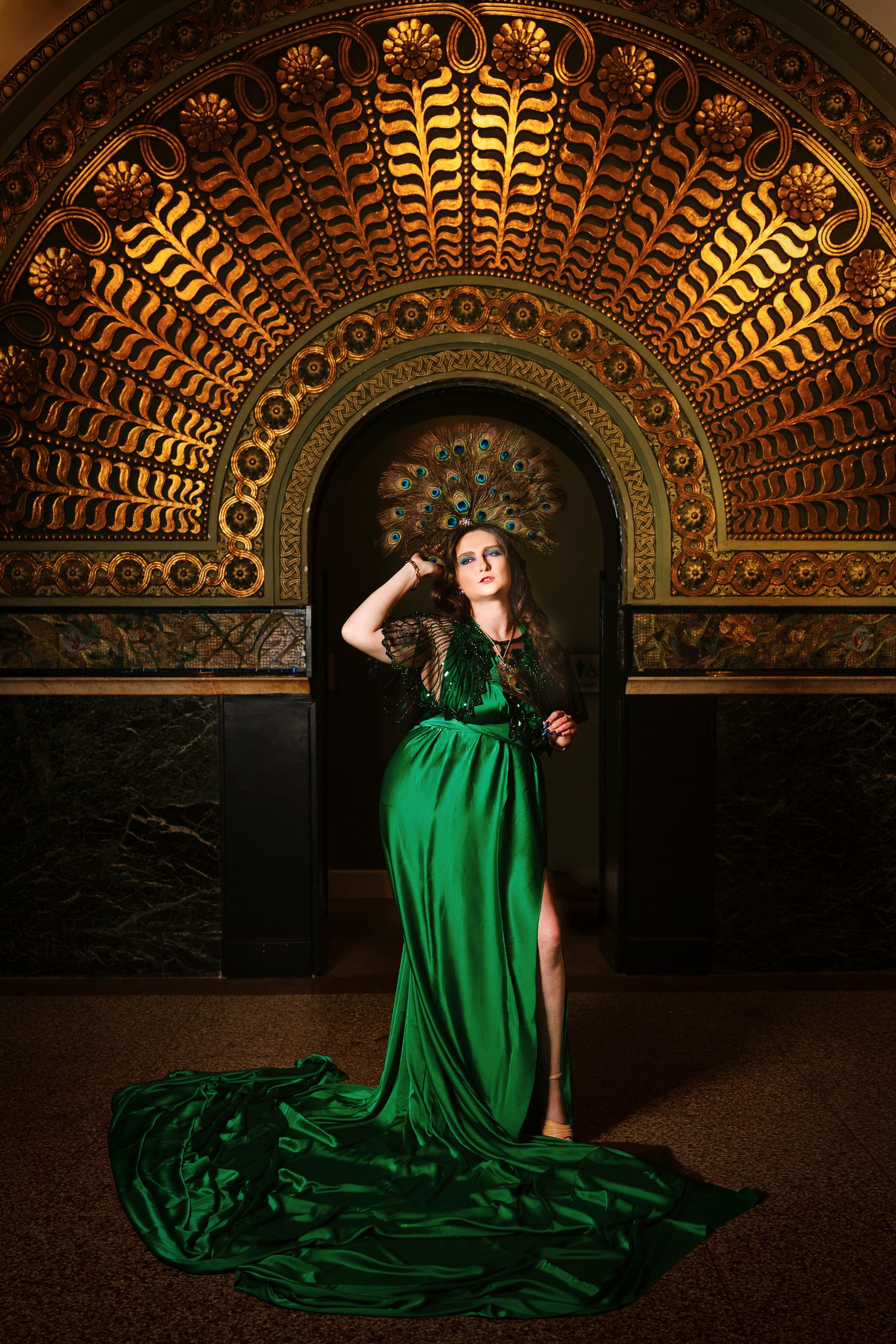 Wollongong Portrait Photographer. Woman in elegant green gown poses before ornate golden arch with intricate Art Deco patterns.
