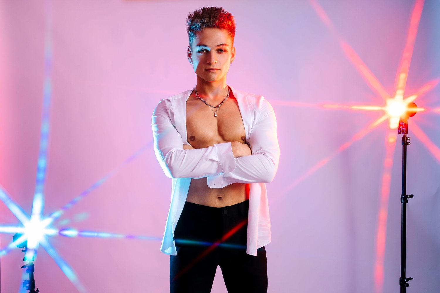 Wollongong Portrait Photographer. Young man posing shirtless in open white shirt with arms crossed under colorful studio lights.