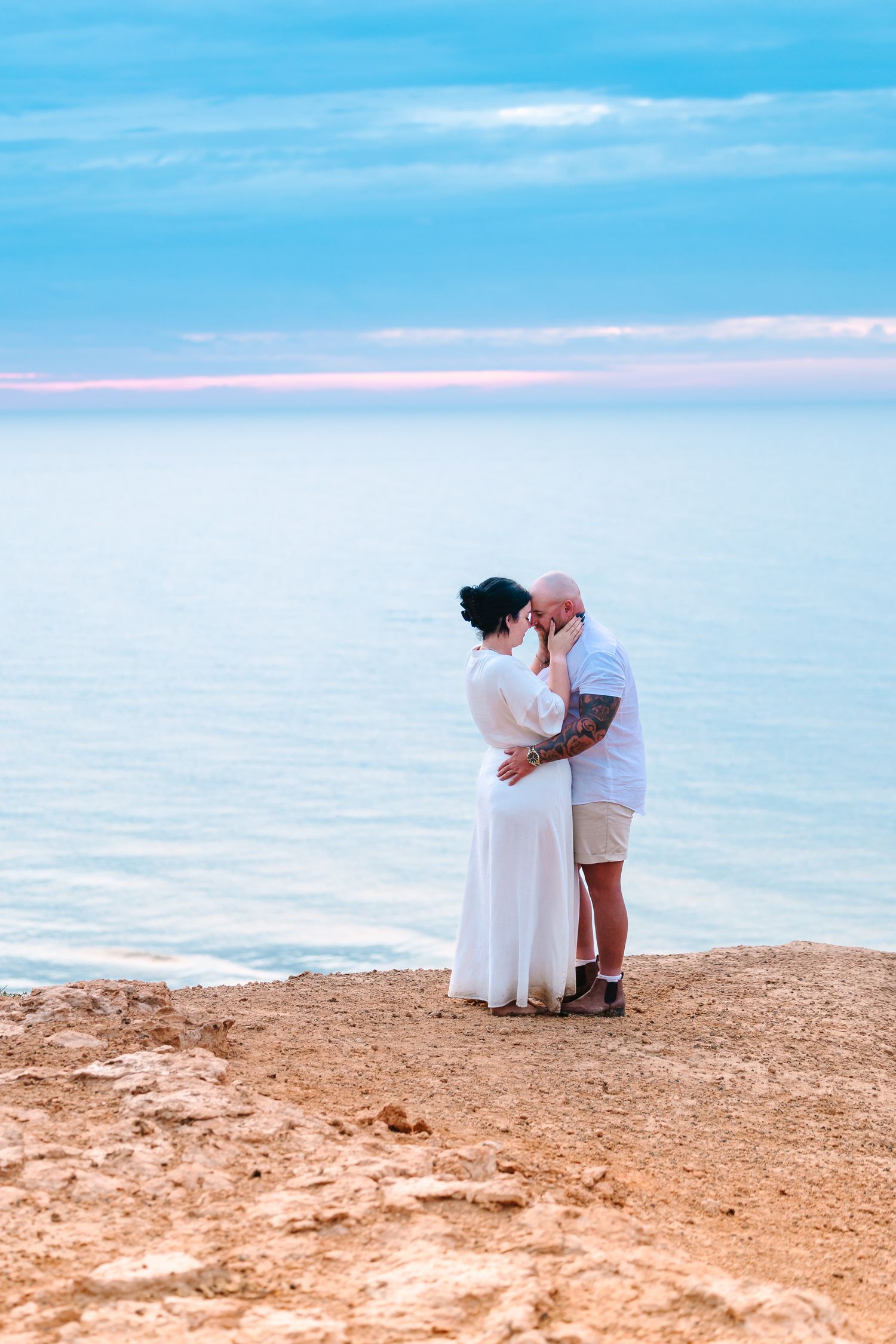 Wollongong Couples and Engagement Photographer. Couple kissing on cliff with azure ocean behind them.