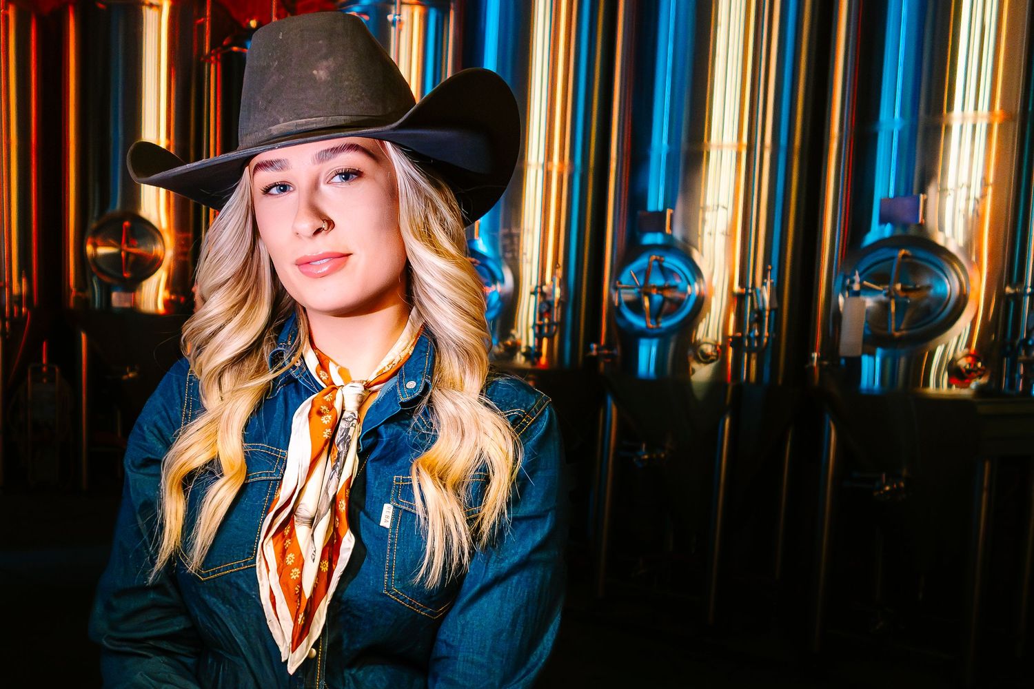Kiana Tomic in cowboy hat and denim jacket with scarf poses before shiny brewery tanks. Wollongong Personal Branding Photography