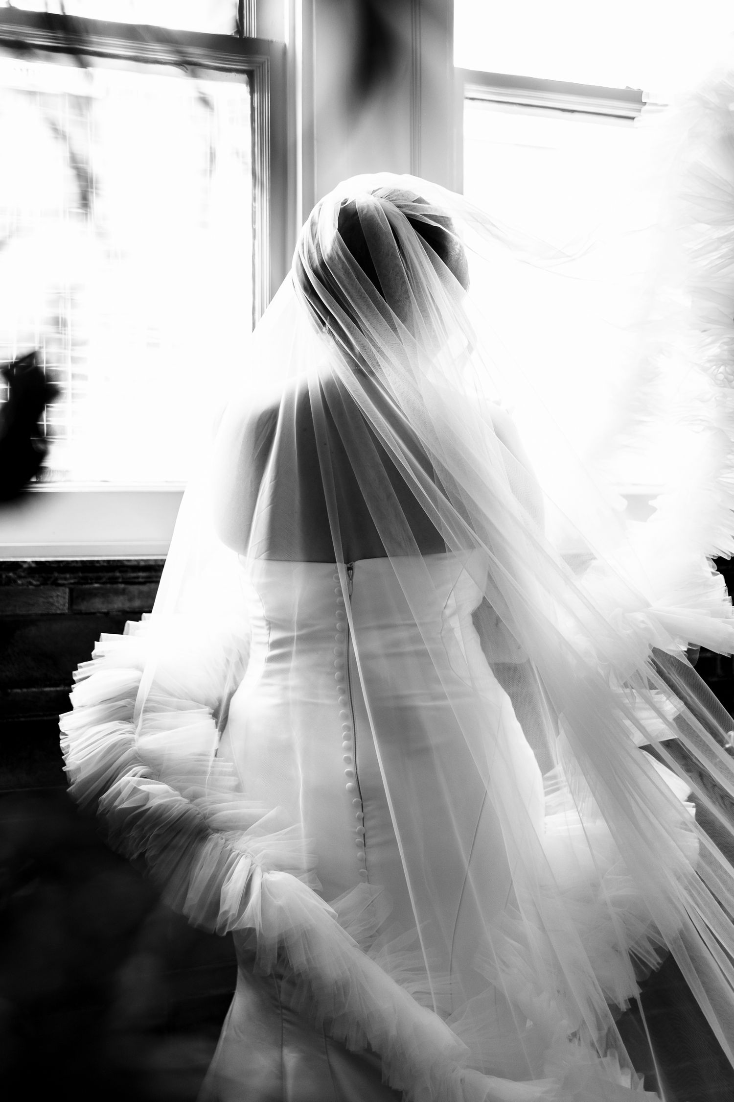 Wollongong Wedding Photographer. Black and white photo of a bride in a white gown and veil standing near a bright window on her wedding day.