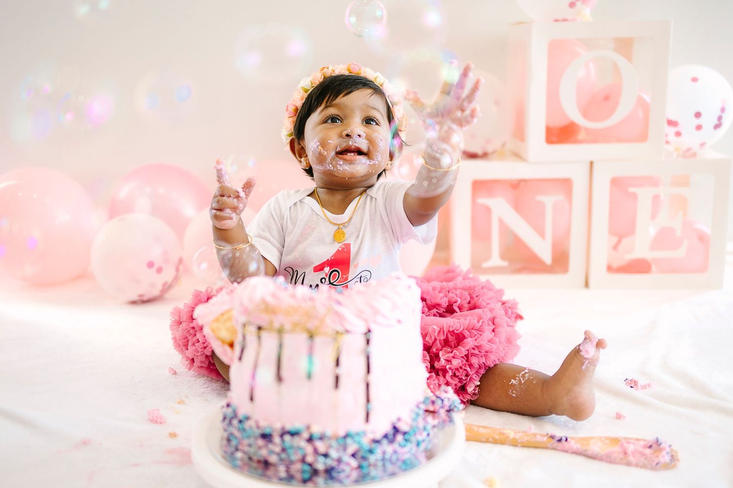 Baby girl celebrates first birthday smashing pink cake, sitting near ONE blocks and pink balloons. Wollongong Portrait Photographer