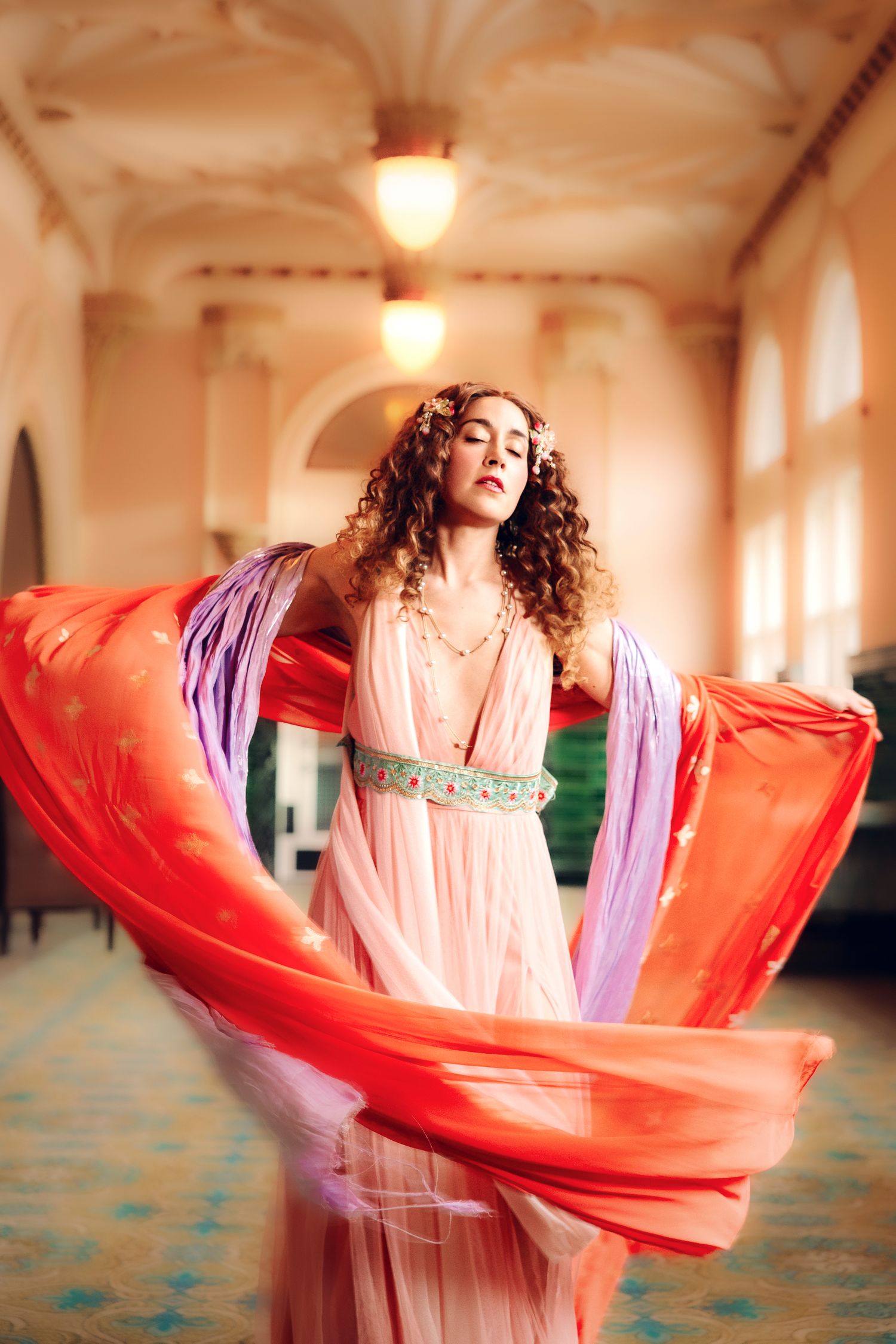 Wollongong Portrait Photographer. A woman in a flowing pink dress with red and purple fabric swirling around her in an ornate golden hall.