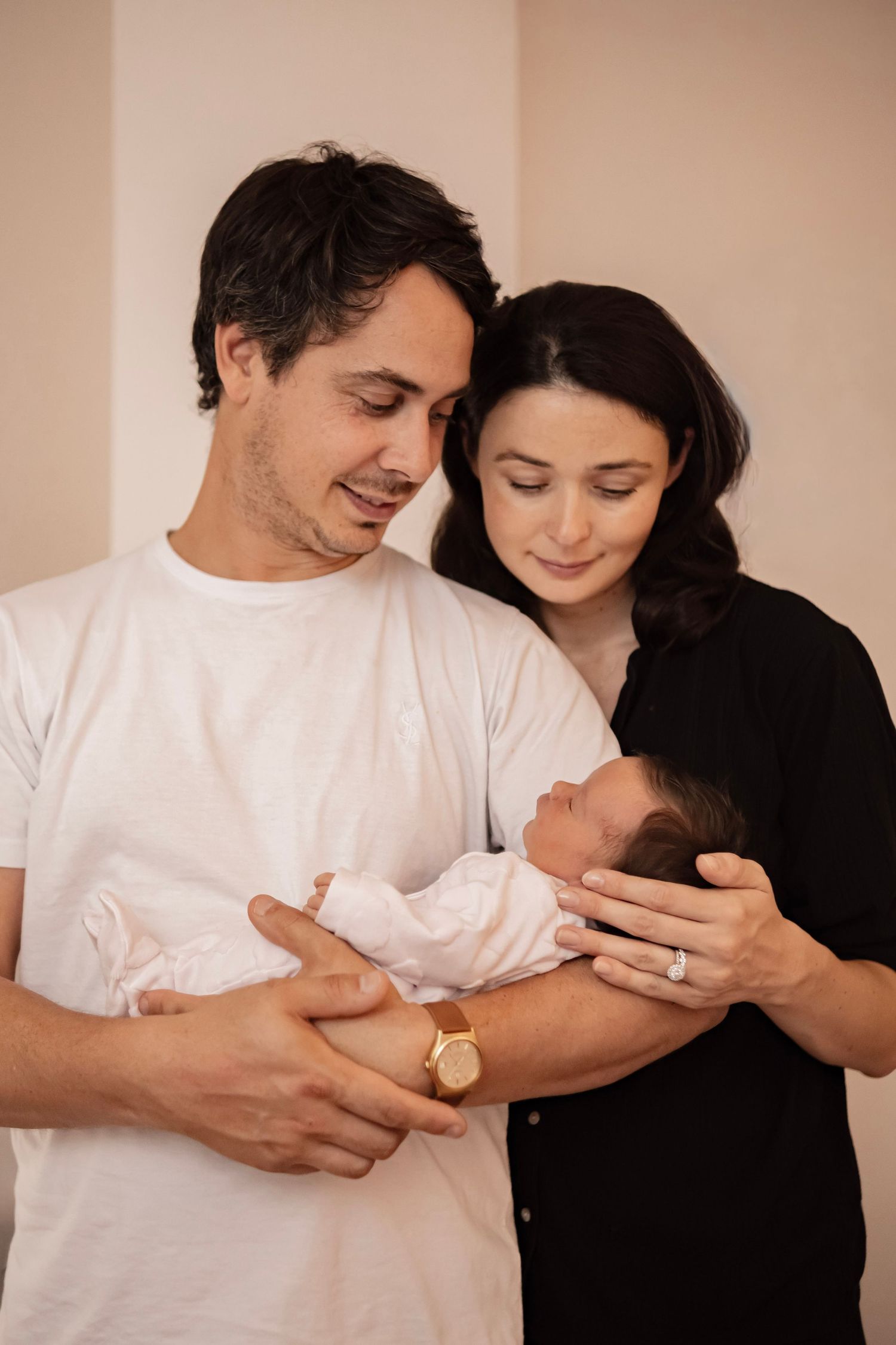Happy parents holding their newborn baby, smiling lovingly in a warm, softly lit indoor setting.