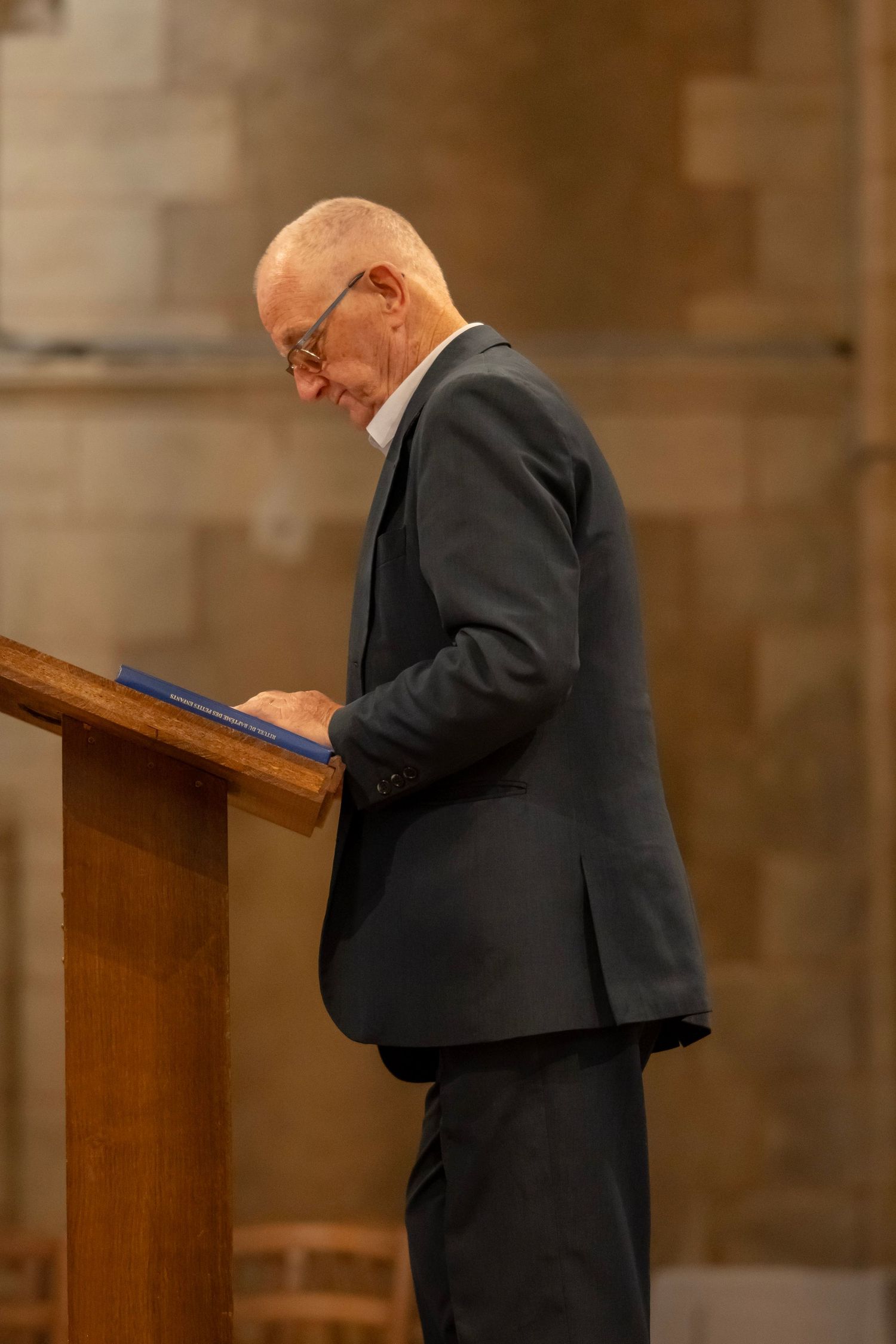 Senior man in a dark suit reading from a podium during a formal event.