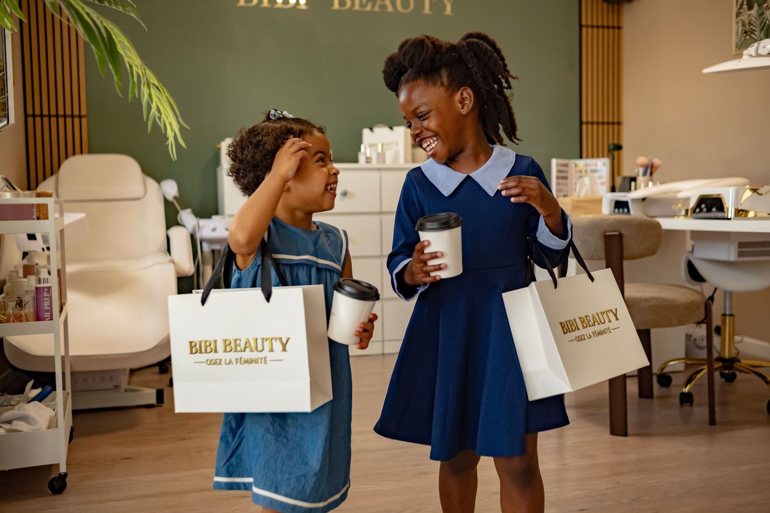 Two young girls smiling and holding Bibi Beauty shopping bags inside a beauty salon.