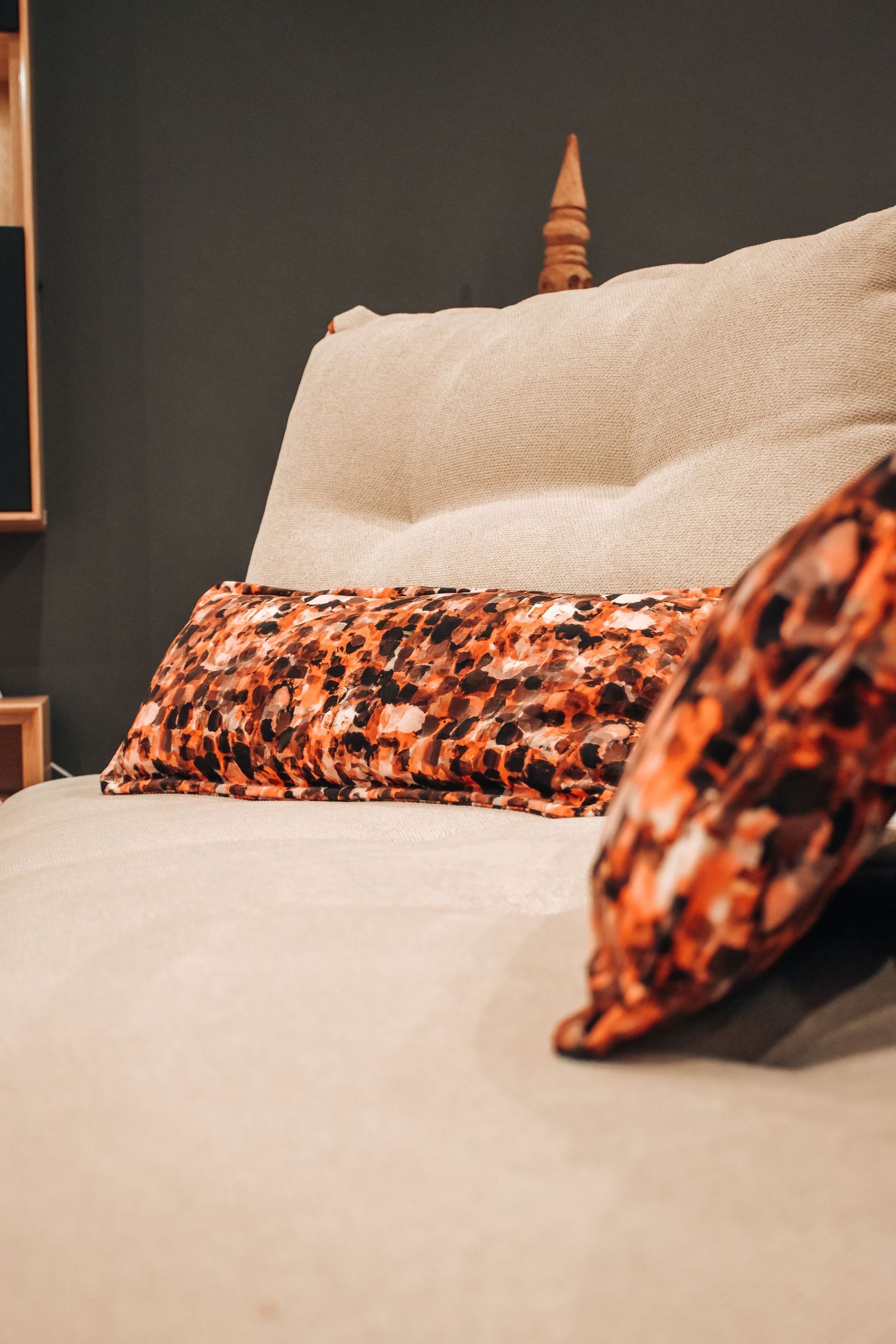 A white bed decorated with rustic orange and brown patterned throw pillows against a dark wall.