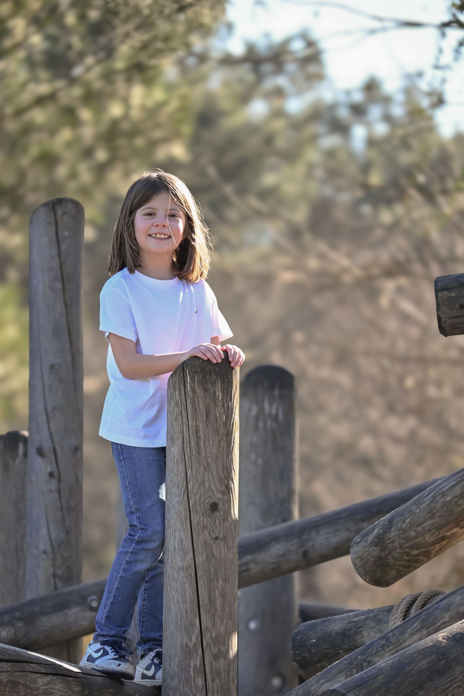 A child in white t-shirt and jeans leans against wooden fence posts outdoors.