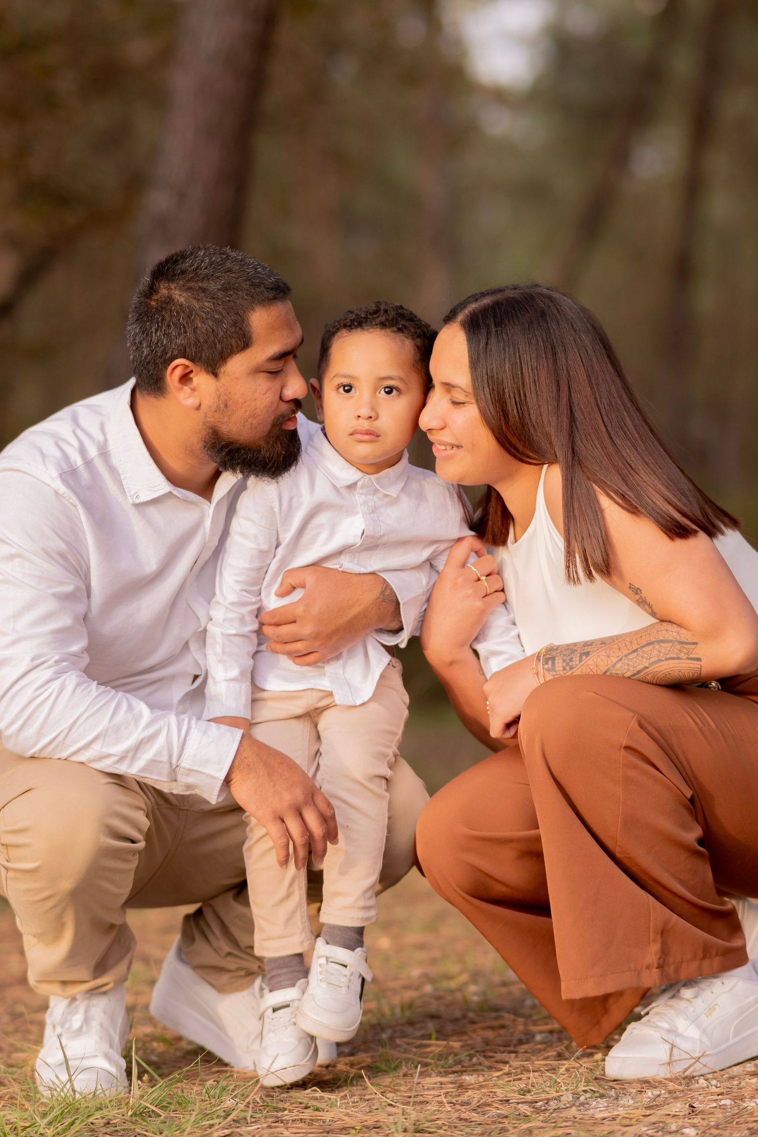 A family in white and brown outfits poses for a series of candid shots outdoors showing loving interactions.