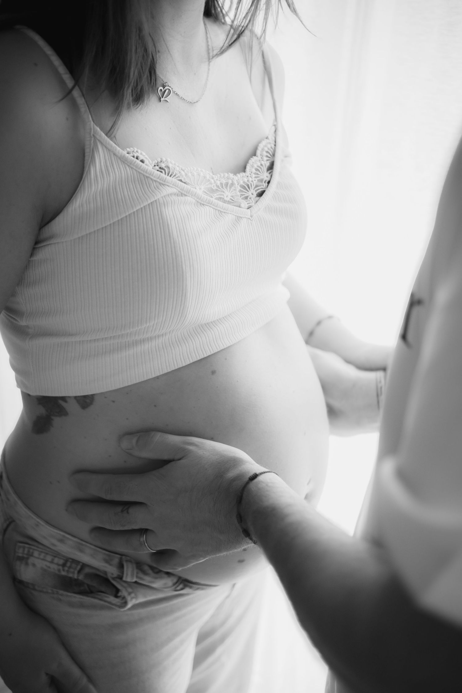 Black and white intimate maternity photo showing hands gently cradling a pregnant belly in soft natural light.