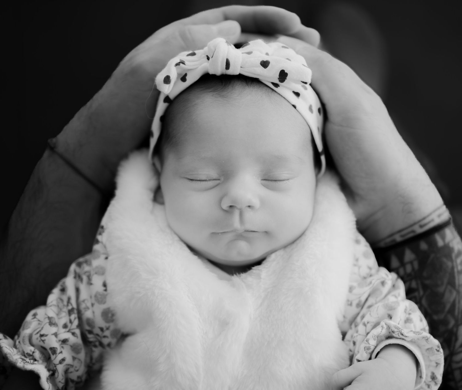 A sleeping baby wearing a polka dot hat and white lace clothing is captured in a black and white photograph.